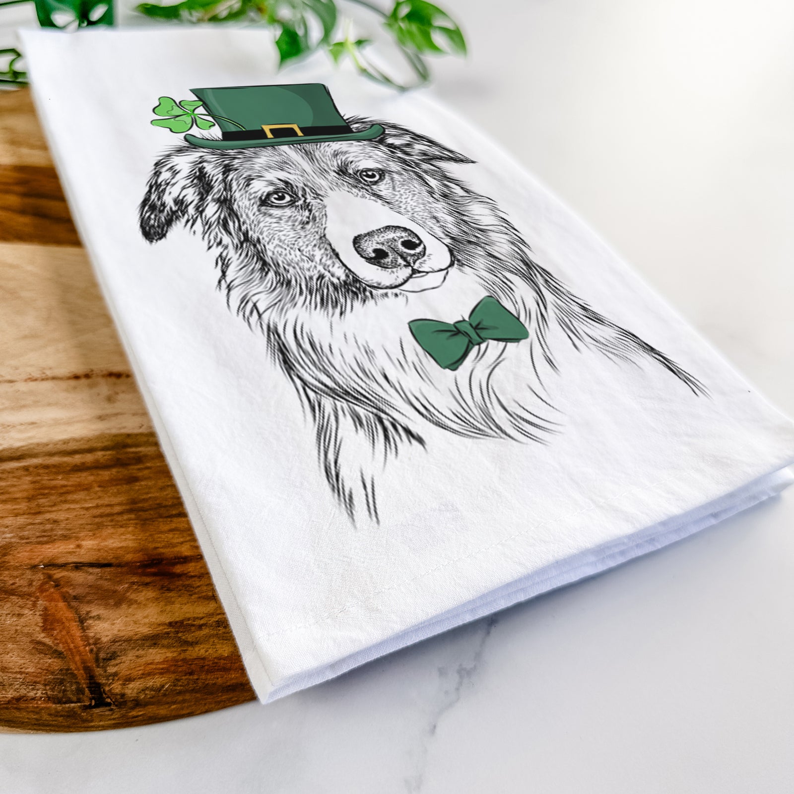 Hand-drawn sketch of Cynder the English Shepherd wearing a St. Patrick's Day leprechaun hat and bow tie on a tea towel