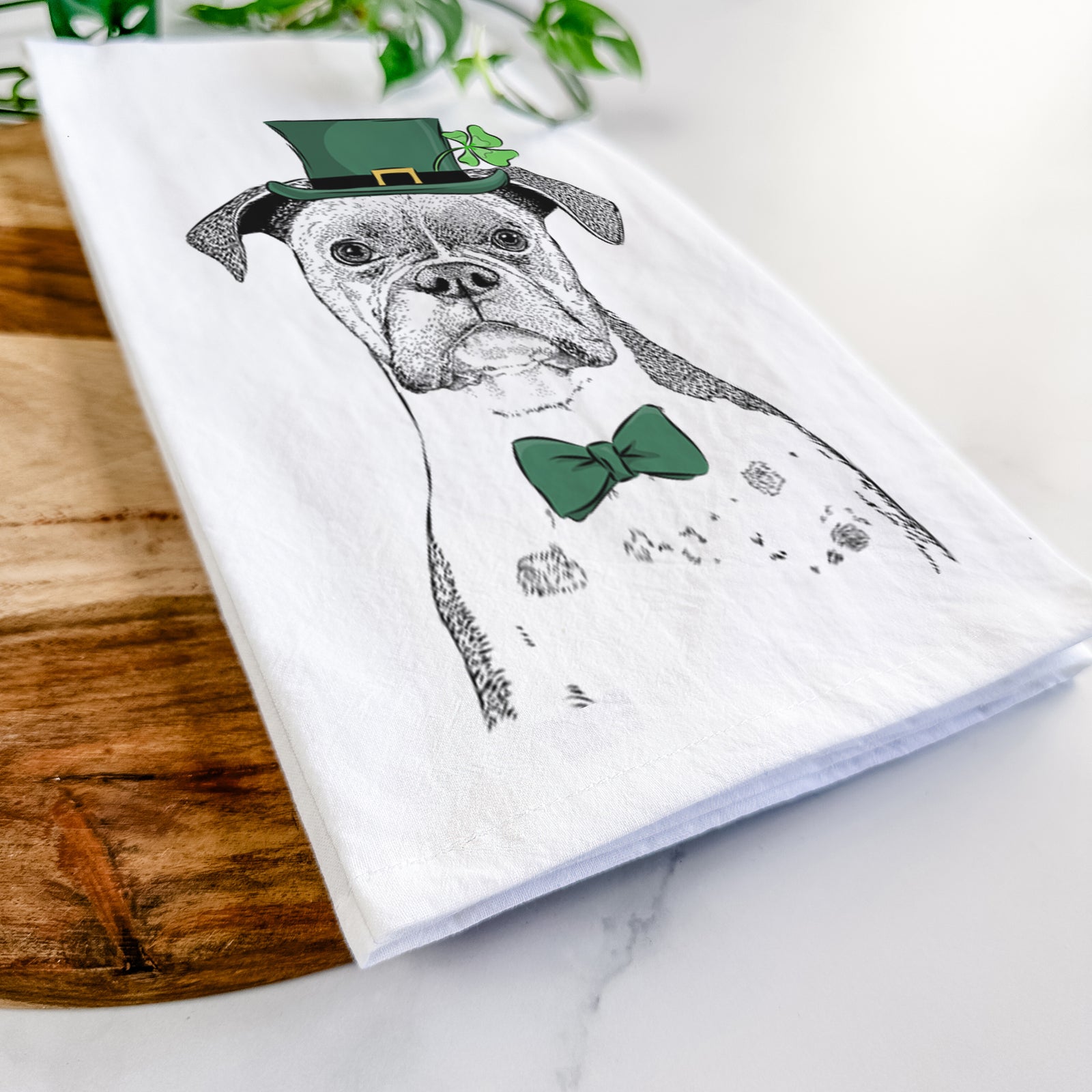 Hand-drawn sketch of Daisy the Boxer wearing a St. Patrick's Day leprechaun hat and bow tie on a tea towel