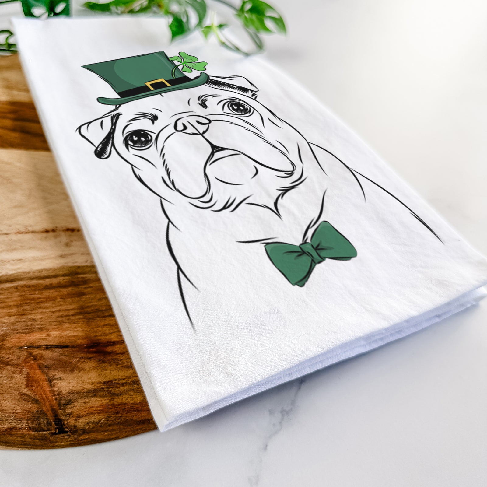 Hand-drawn sketch of Darling Chloe the Pug wearing a St. Patrick's Day leprechaun hat and bow tie on a tea towel