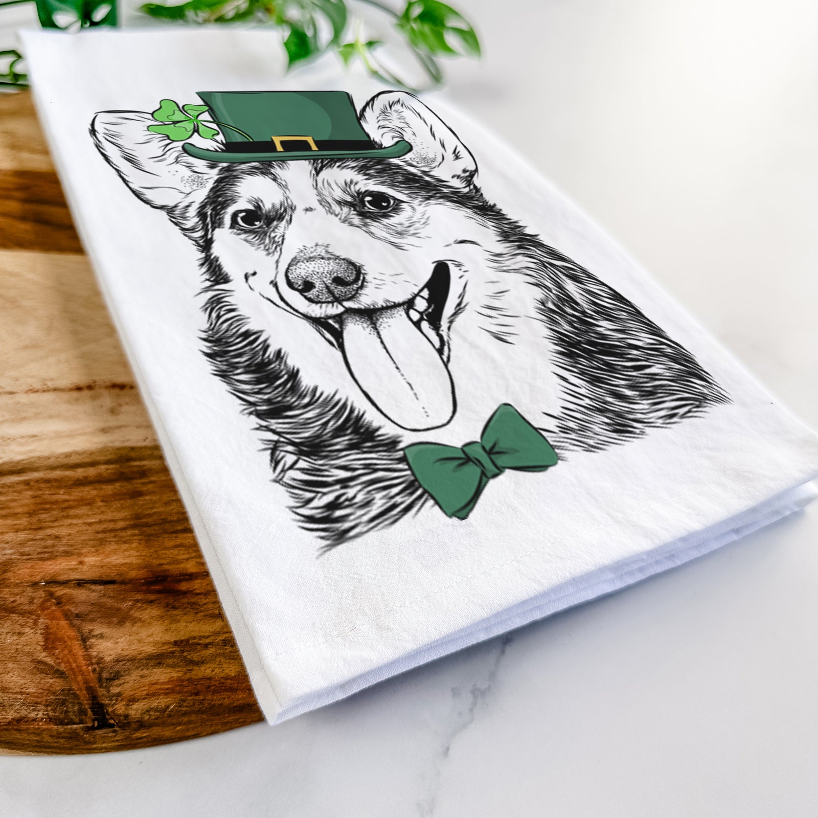 Hand-drawn sketch of Darma the Corgi wearing a St. Patrick's Day leprechaun hat and bow tie on a tea towel