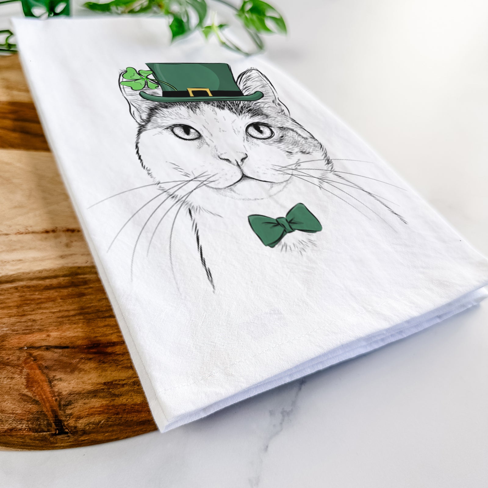 Hand-drawn sketch of Denver the Calico Cat wearing a St. Patrick's Day leprechaun hat and bow tie on a tea towel