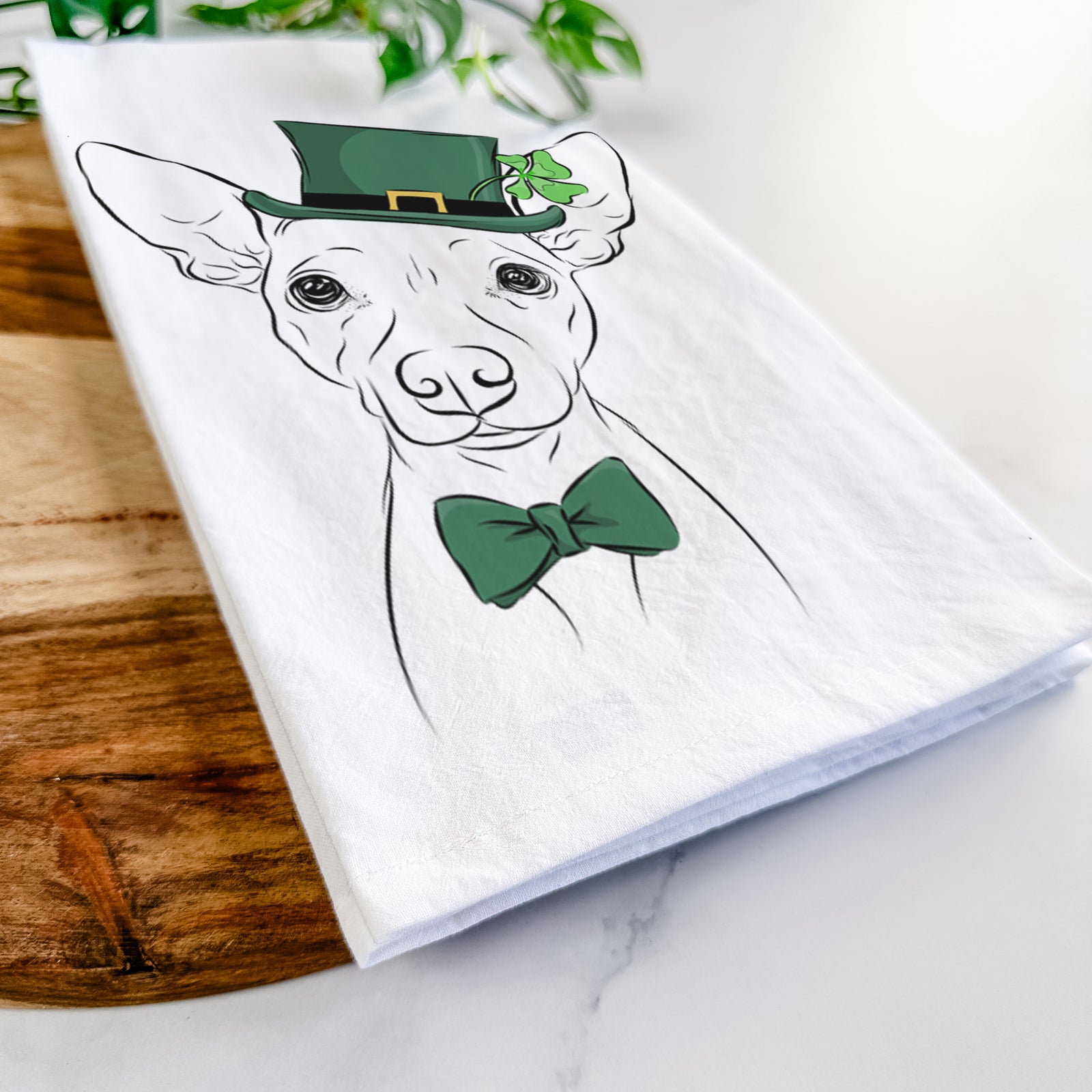 Hand-drawn sketch of Desi the American Hairless Terrier wearing a St. Patrick's Day leprechaun hat and bow tie on a tea towel