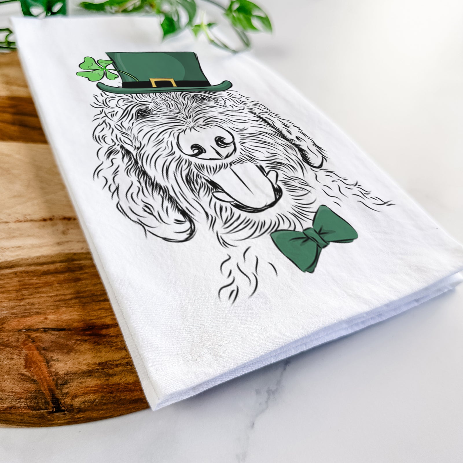 Hand-drawn sketch of Dixie the Doodle wearing a St. Patrick's Day leprechaun hat and bow tie on a tea towel
