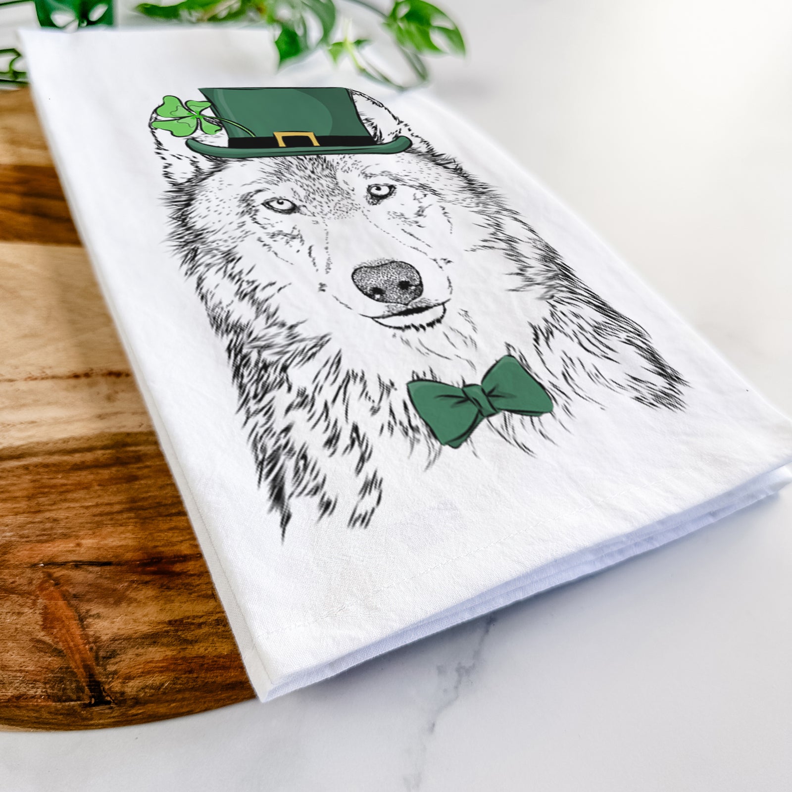 Hand-drawn sketch of Django the Grey Wolf wearing a St. Patrick's Day leprechaun hat and bow tie on a tea towel