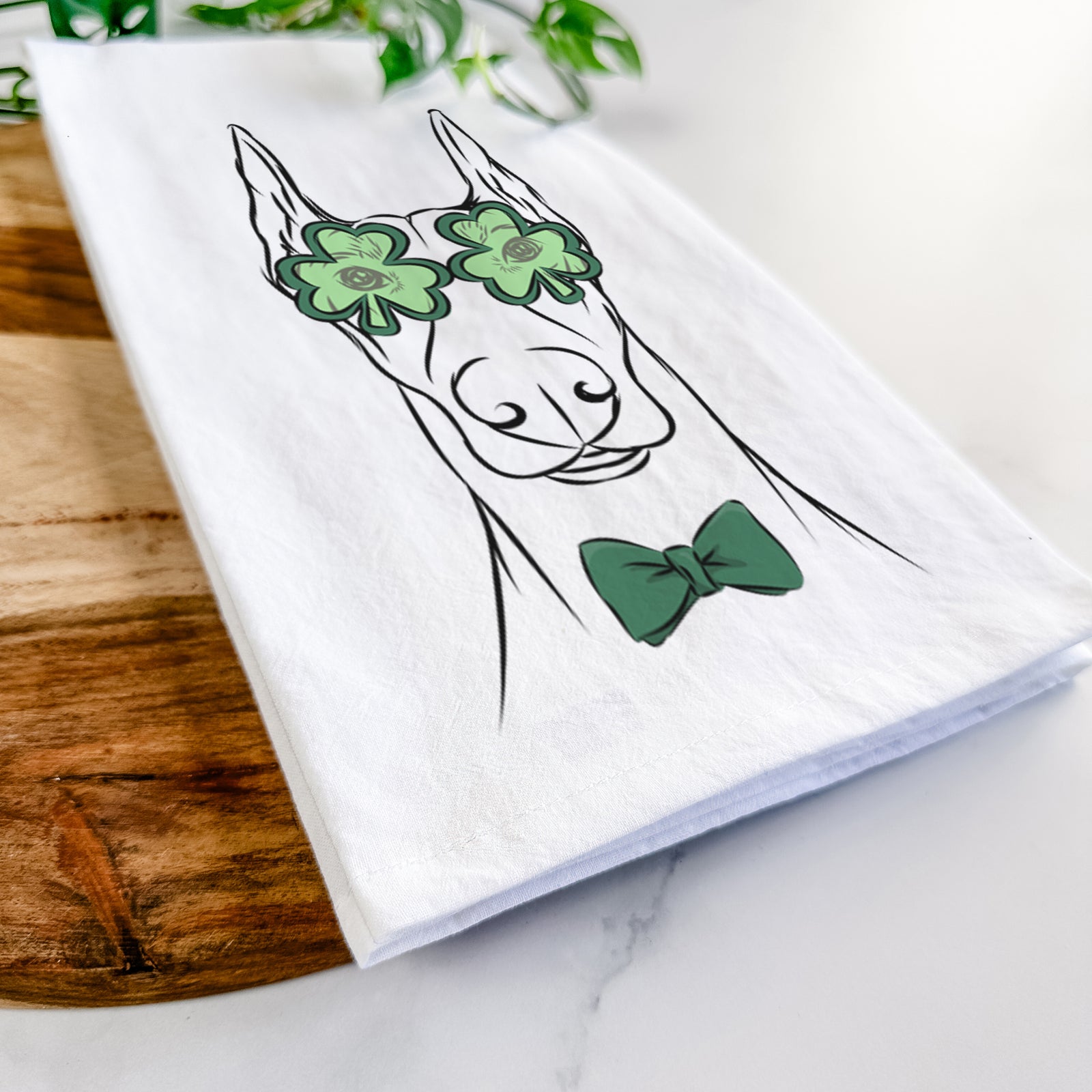 Hand-drawn sketch of Duke the Doberman Pinscher wearing a St. Patrick's Day leprechaun hat and bow tie on a tea towel