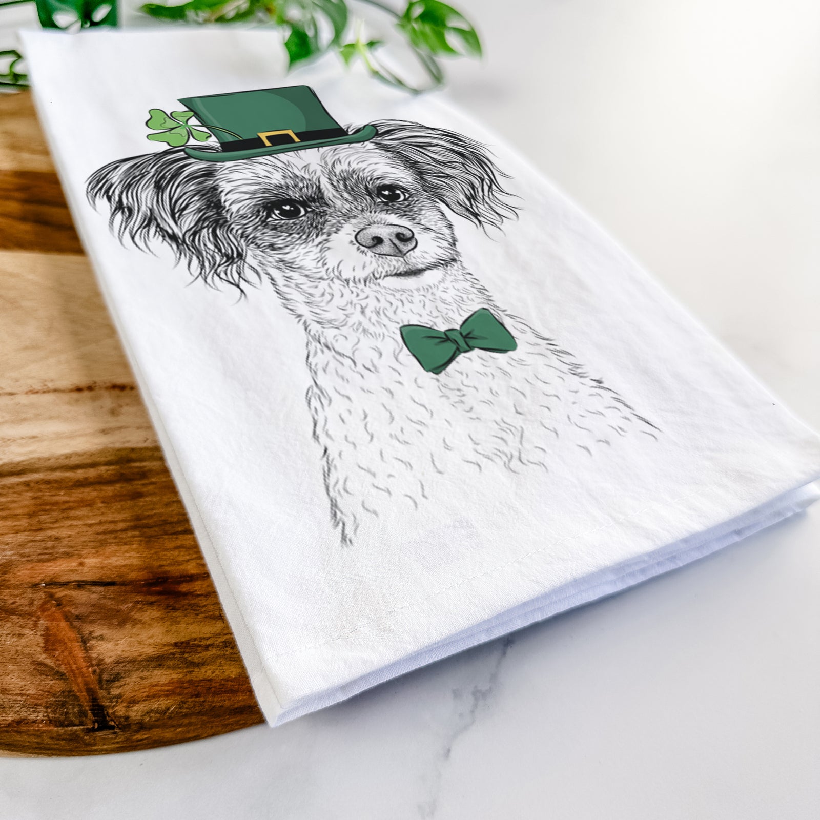 Hand-drawn sketch of Finley the Papillon Mix wearing a St. Patrick's Day leprechaun hat and bow tie on a tea towel