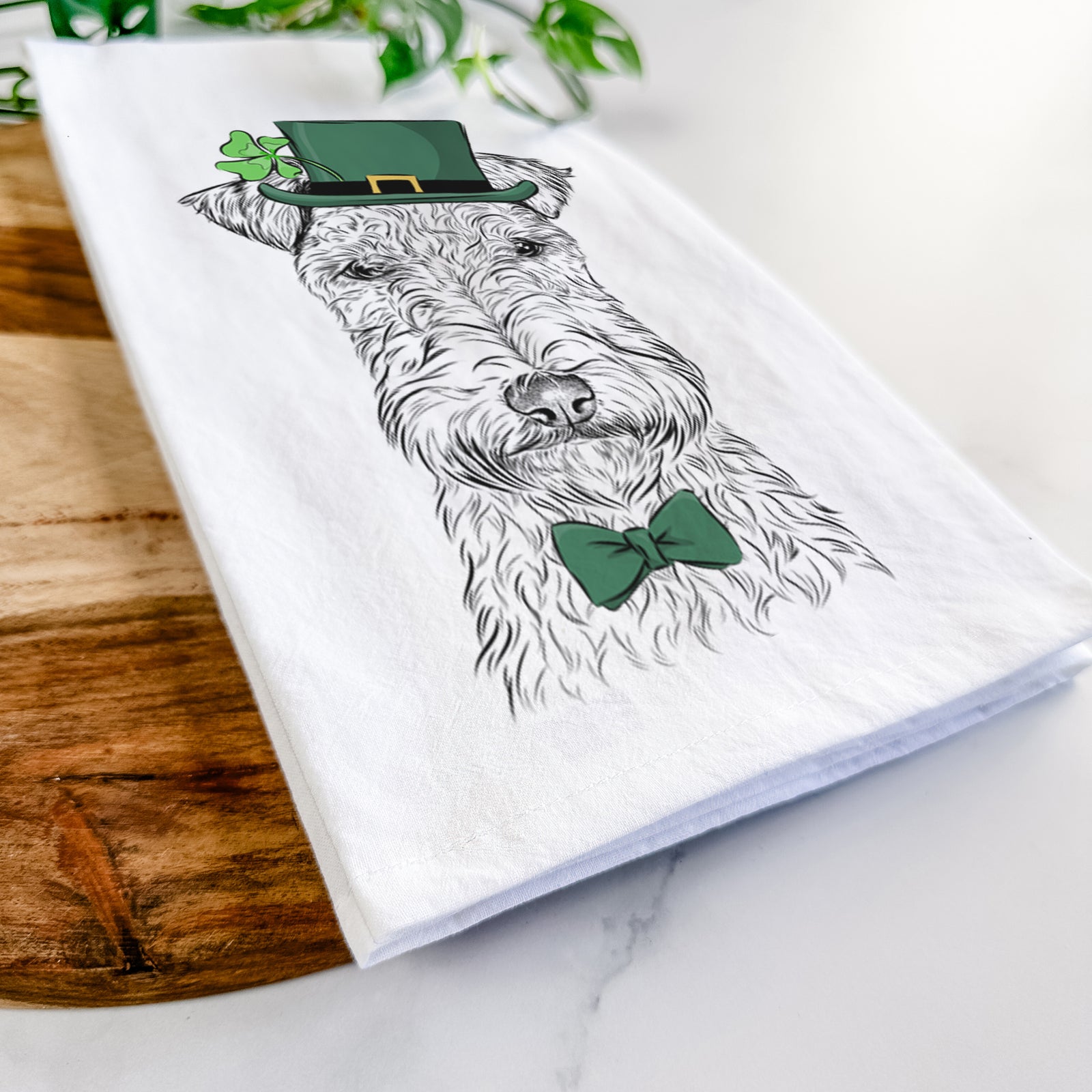Hand-drawn sketch of Frida the Lakeland Terrier wearing a St. Patrick's Day leprechaun hat and bow tie on a tea towel
