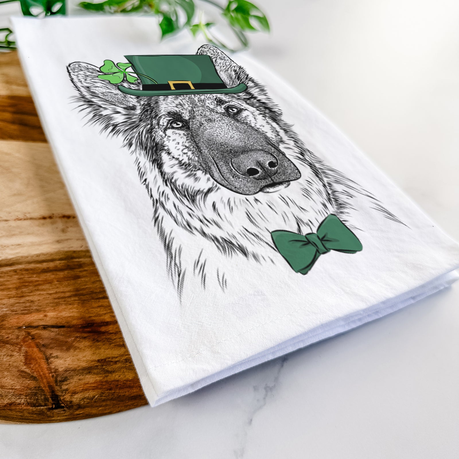 Hand-drawn sketch of Geddy the Shiloh Shepherd wearing a St. Patrick's Day leprechaun hat and bow tie on a tea towel