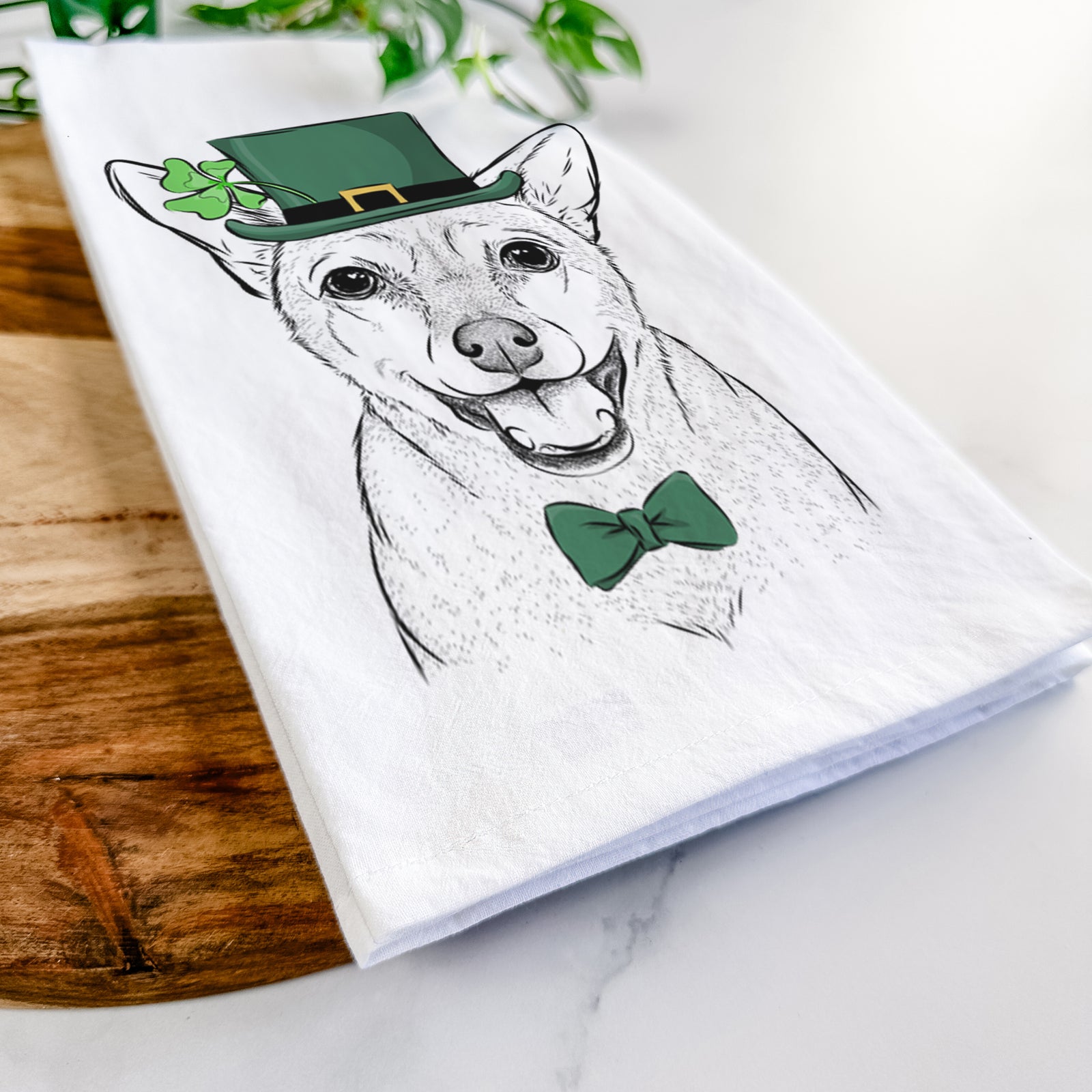 Hand-drawn sketch of Georgie the Chiweenie wearing a St. Patrick's Day leprechaun hat and bow tie on a tea towel
