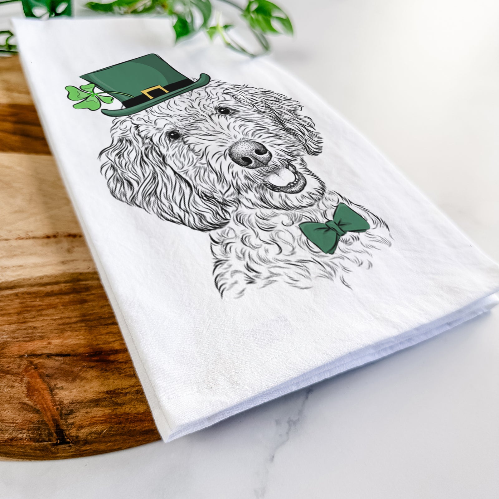 Hand-drawn sketch of Gizmo the Goldendoodle wearing a St. Patrick's Day leprechaun hat and bow tie on a tea towel