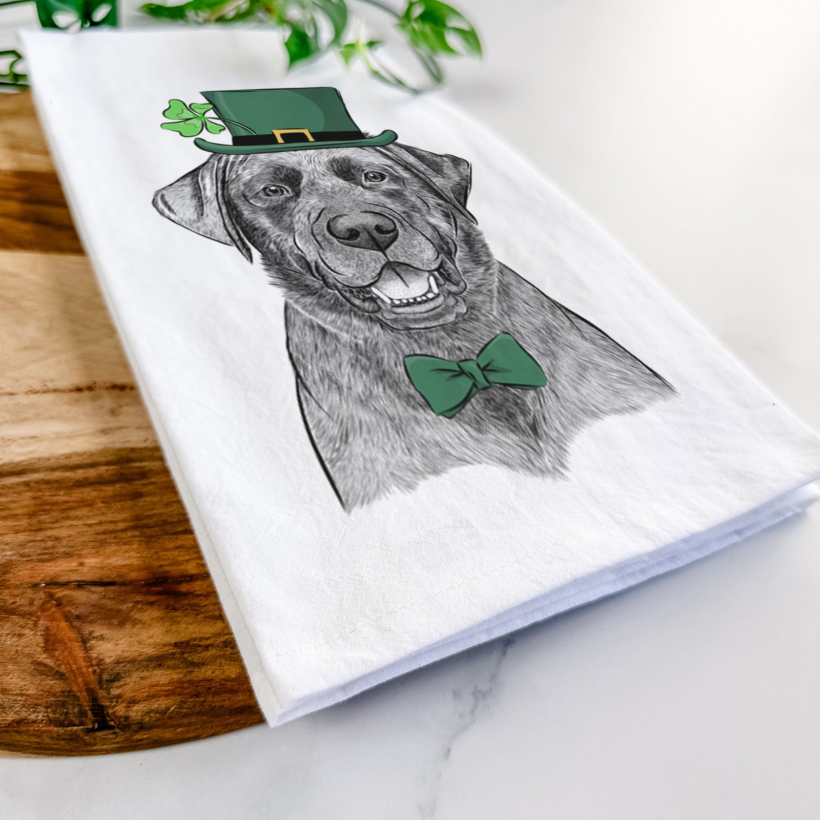 Hand-drawn sketch of Heath the Black Lab wearing a St. Patrick's Day leprechaun hat and bow tie on a tea towel