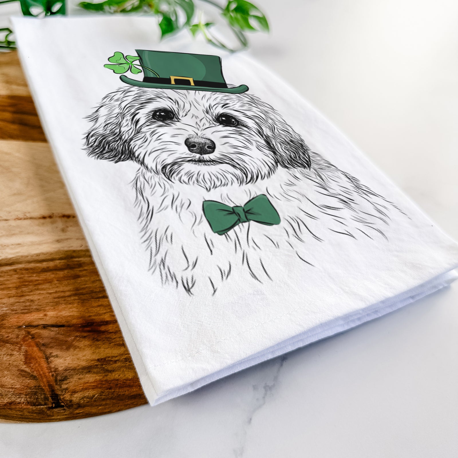 Hand-drawn sketch of Henry the Havanese wearing a St. Patrick's Day leprechaun hat and bow tie on a tea towel