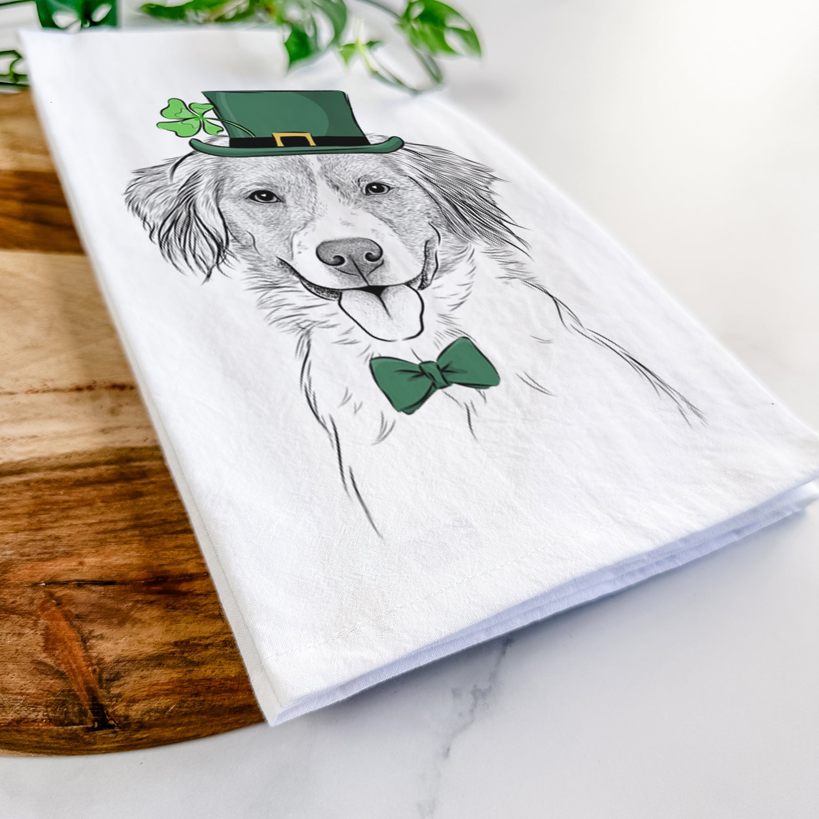 Hand-drawn sketch of Hercules the Nederlandse Kooikerhondje wearing a St. Patrick's Day leprechaun hat and bow tie on a tea towel