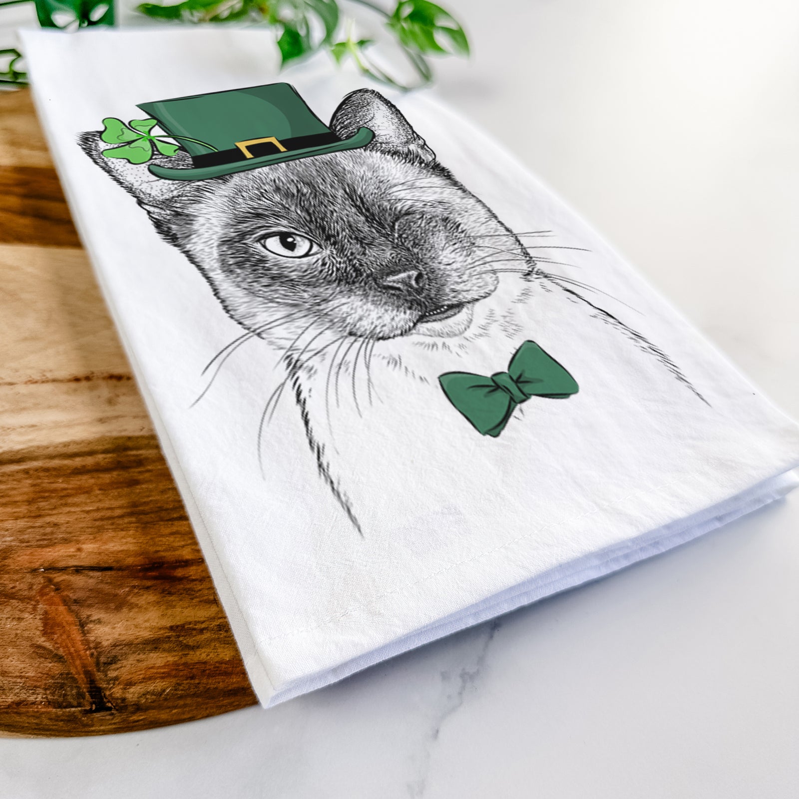 Hand-drawn sketch of Hoggle the Siamese Cat wearing a St. Patrick's Day leprechaun hat and bow tie on a tea towel