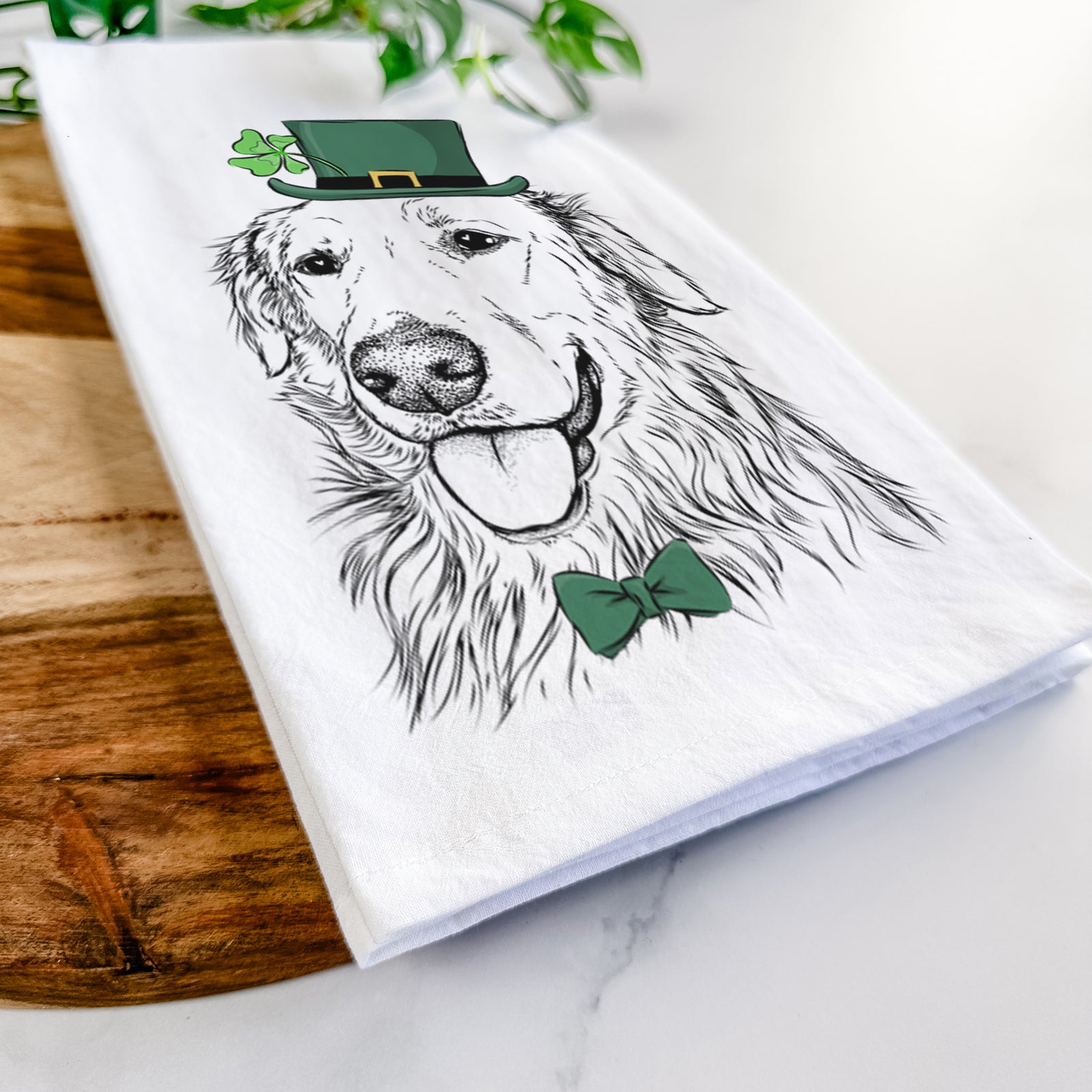Hand-drawn sketch of Hopper the Golden Retriever wearing a St. Patrick's Day leprechaun hat and bow tie on a tea towel