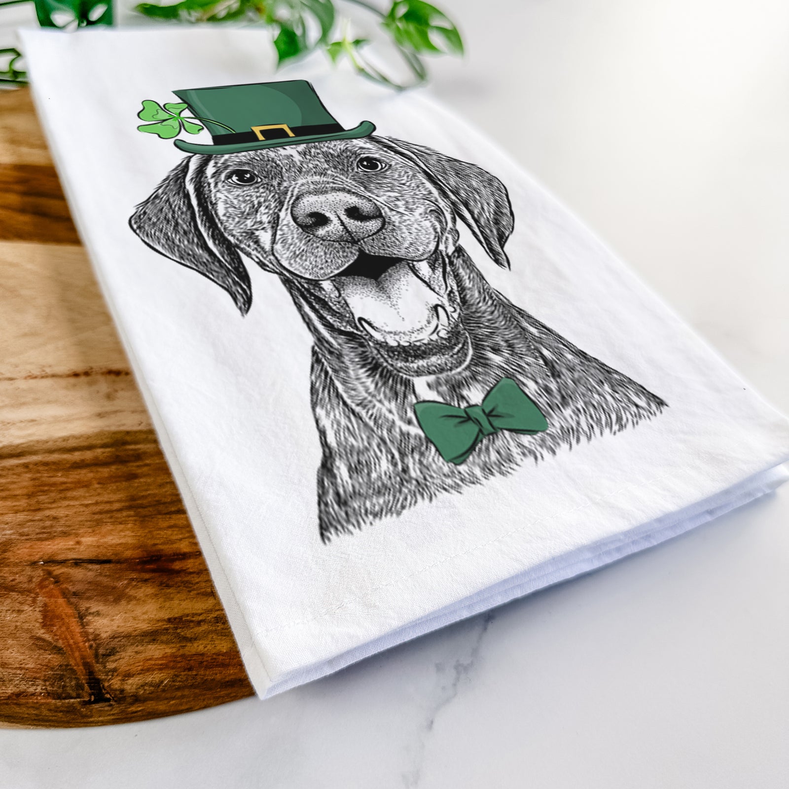 Hand-drawn sketch of Hudson the German Shorthaired Pointer wearing a St. Patrick's Day leprechaun hat and bow tie on a tea towel