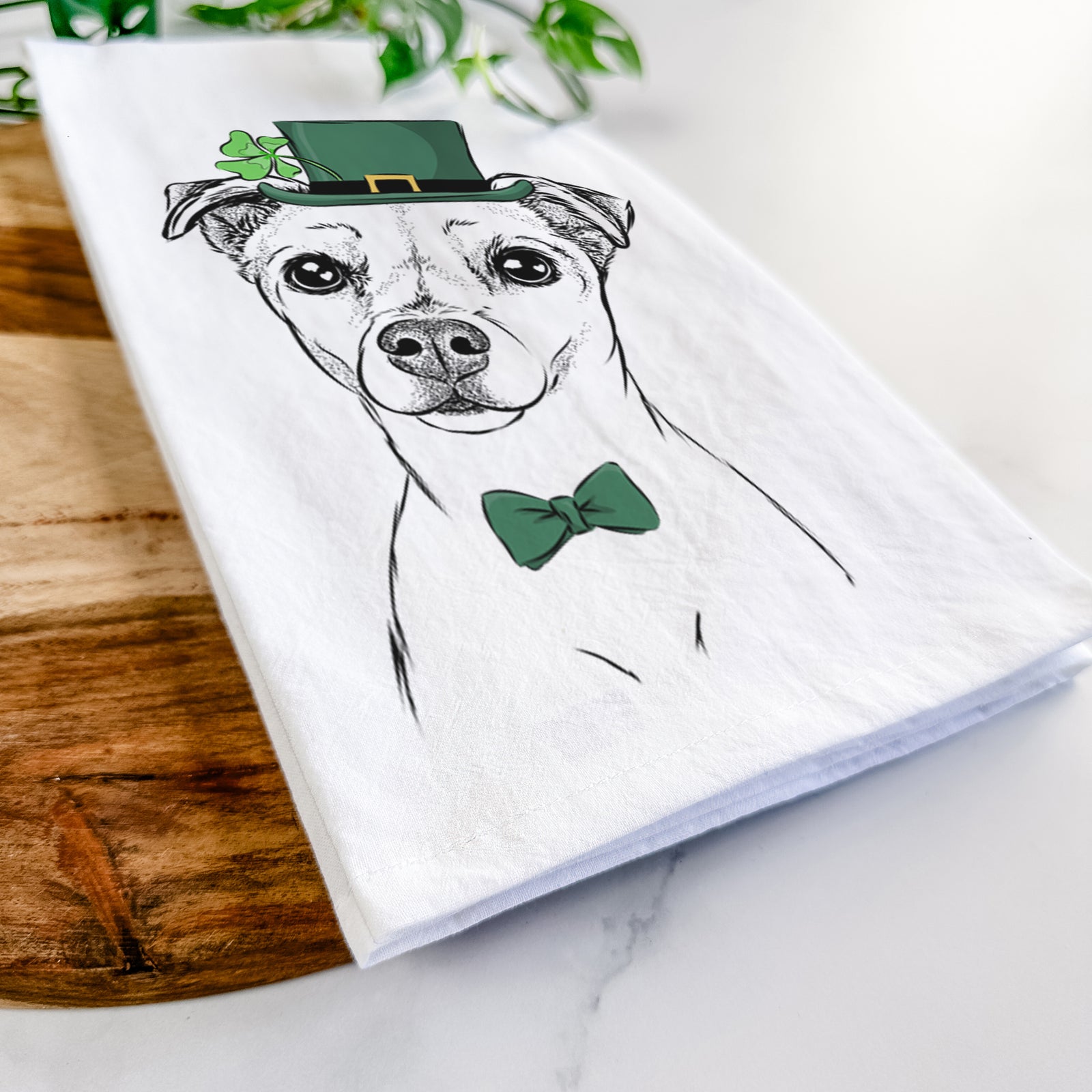 Hand-drawn sketch of Izzy the Chiweenie wearing a St. Patrick's Day leprechaun hat and bow tie on a tea towel