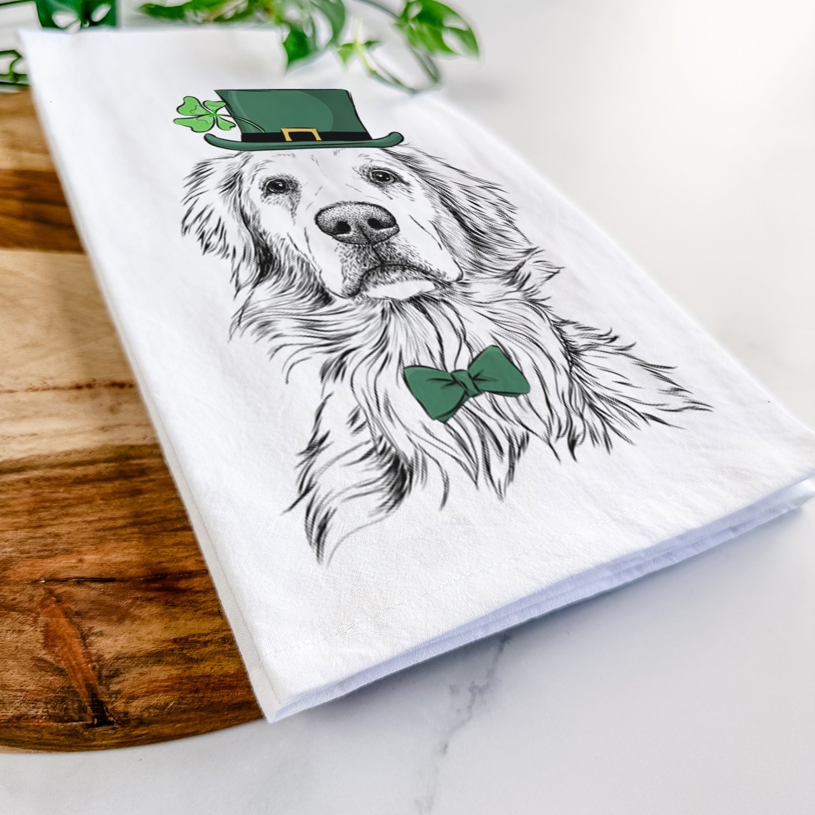 Hand-drawn sketch of Jake aroni the Golden Retriever wearing a St. Patrick's Day leprechaun hat and bow tie on a tea towel