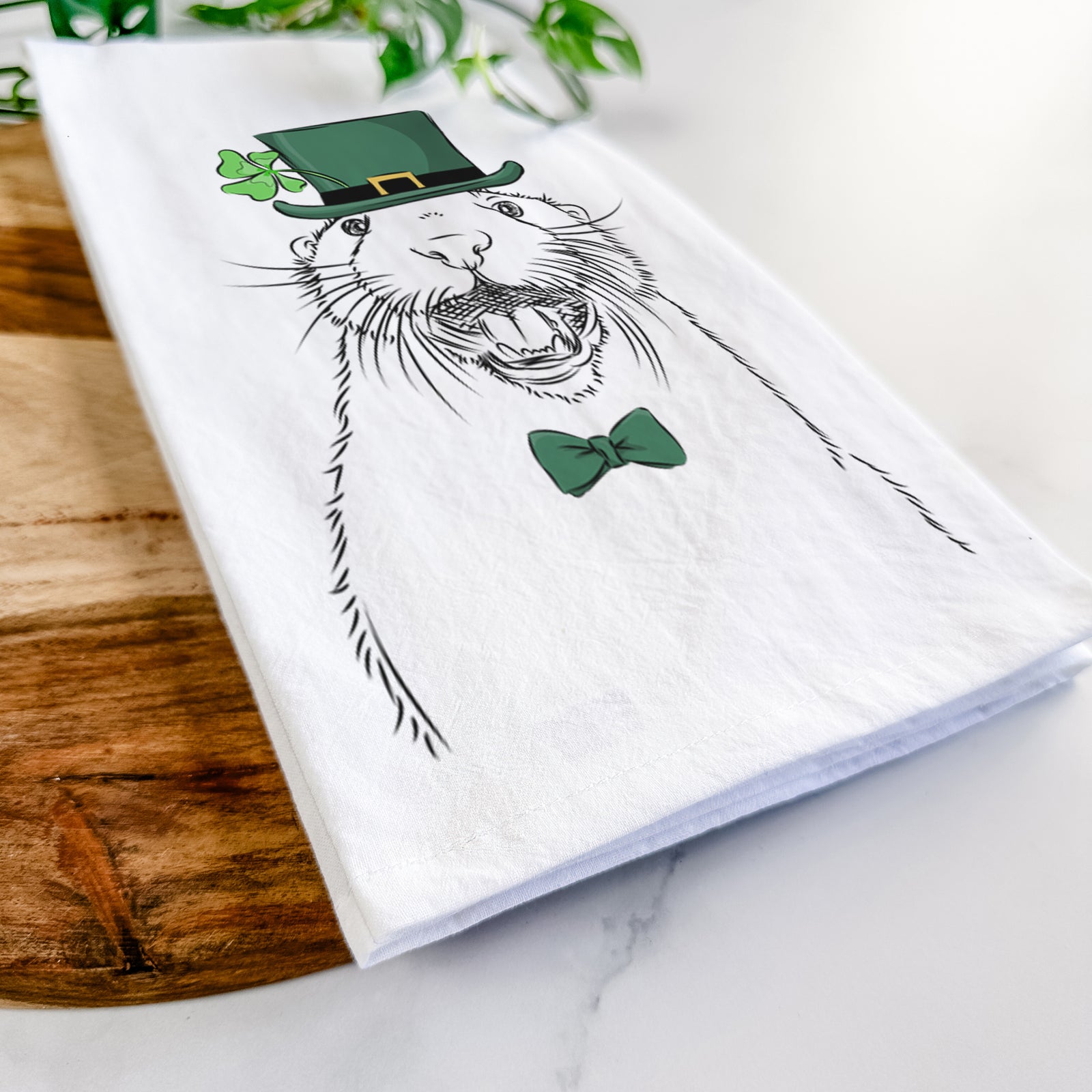 Hand-drawn sketch of Jasper the River Otter wearing a St. Patrick's Day leprechaun hat and bow tie on a tea towel
