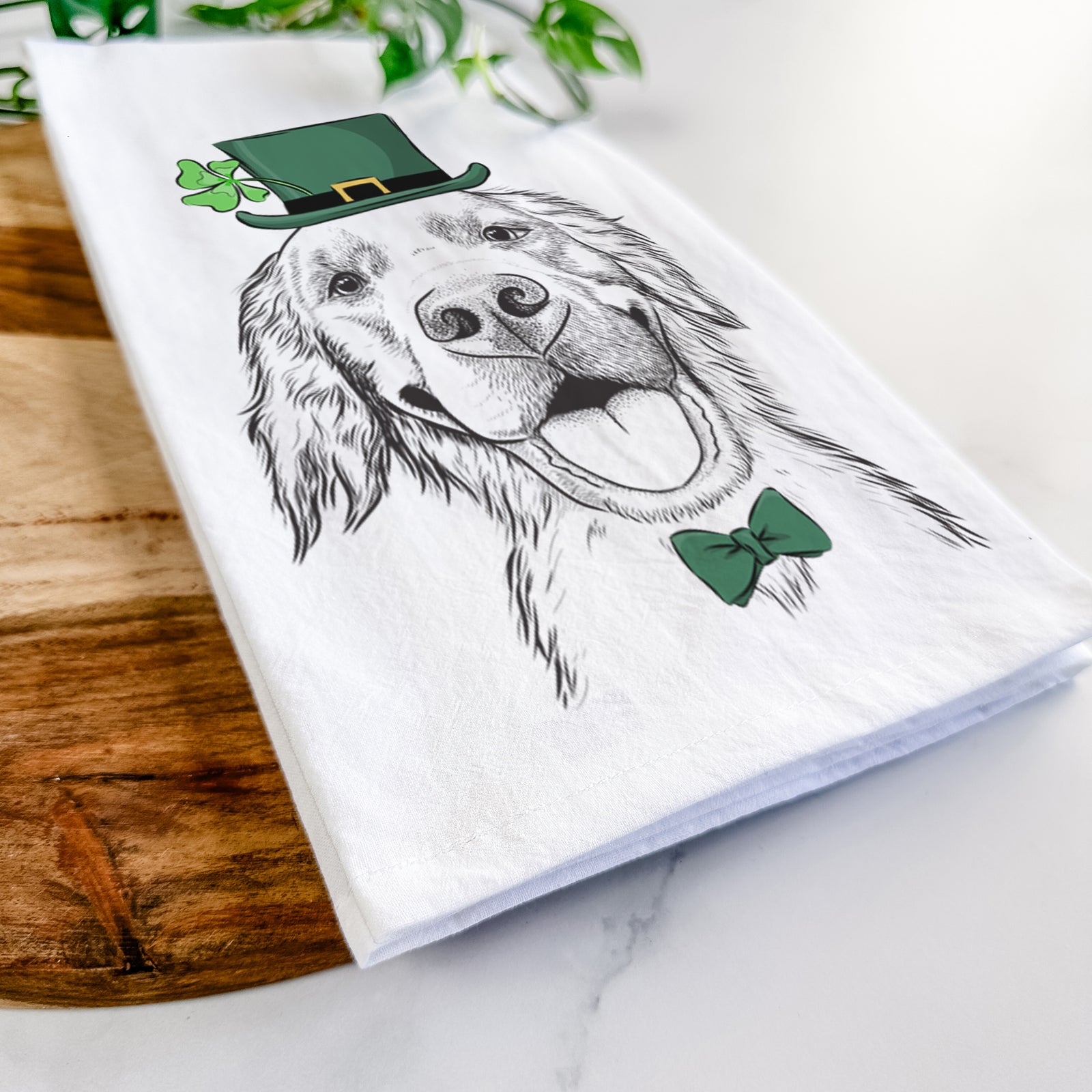 Hand-drawn sketch of Jordy the Golden Retriever wearing a St. Patrick's Day leprechaun hat and bow tie on a tea towel