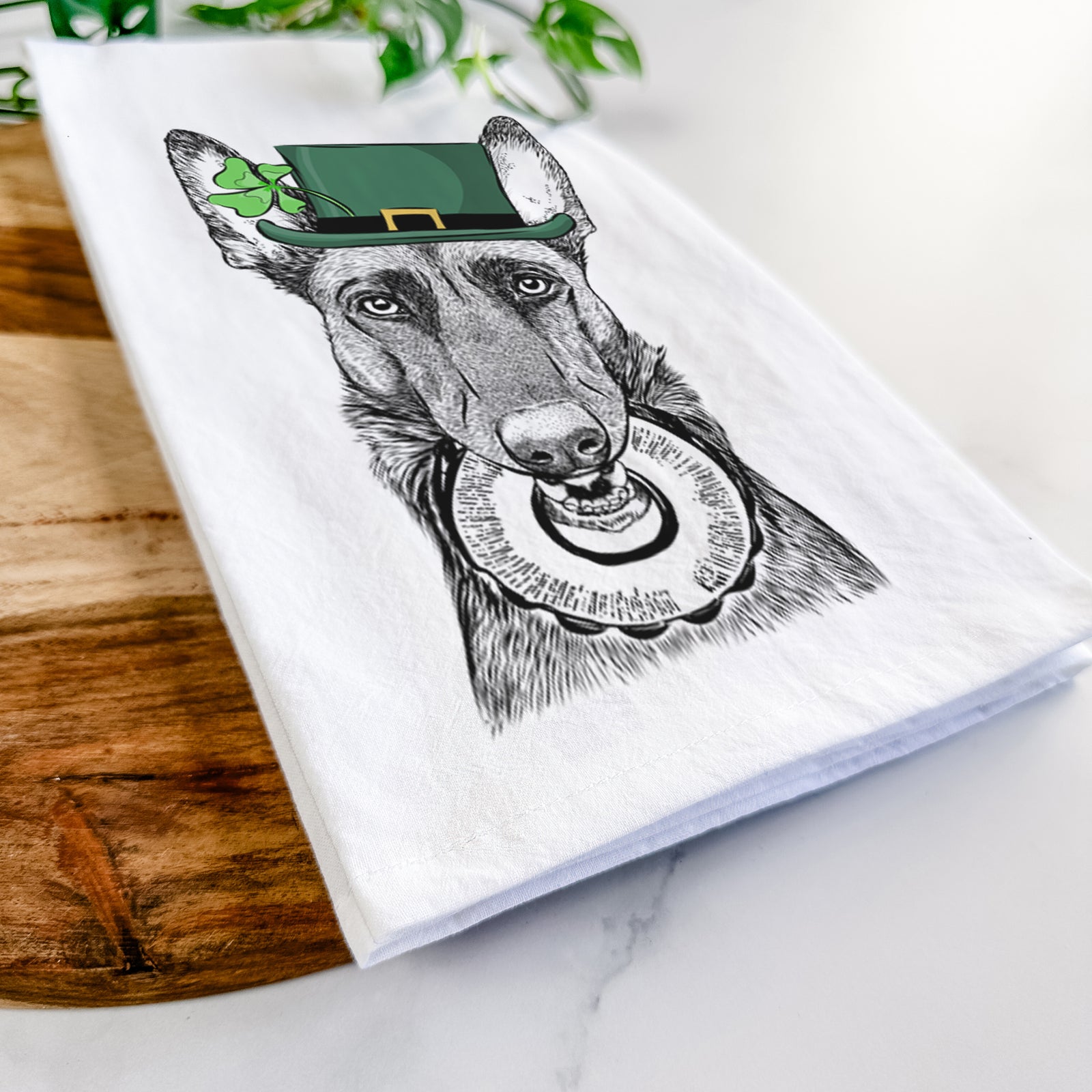 Hand-drawn sketch of Juno the Belgian Malinois wearing a St. Patrick's Day leprechaun hat and bow tie on a tea towel