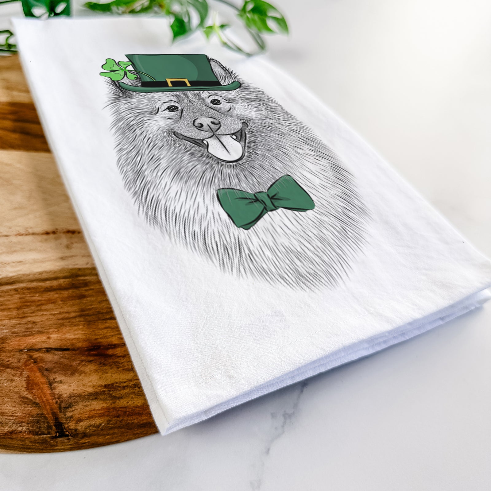 Hand-drawn sketch of Kai the Keeshond wearing a St. Patrick's Day leprechaun hat and bow tie on a tea towel
