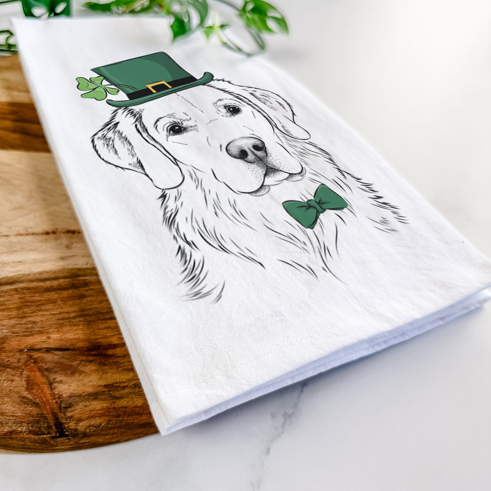 Hand-drawn sketch of Kula the Golden Retriever wearing a St. Patrick's Day leprechaun hat and bow tie on a tea towel