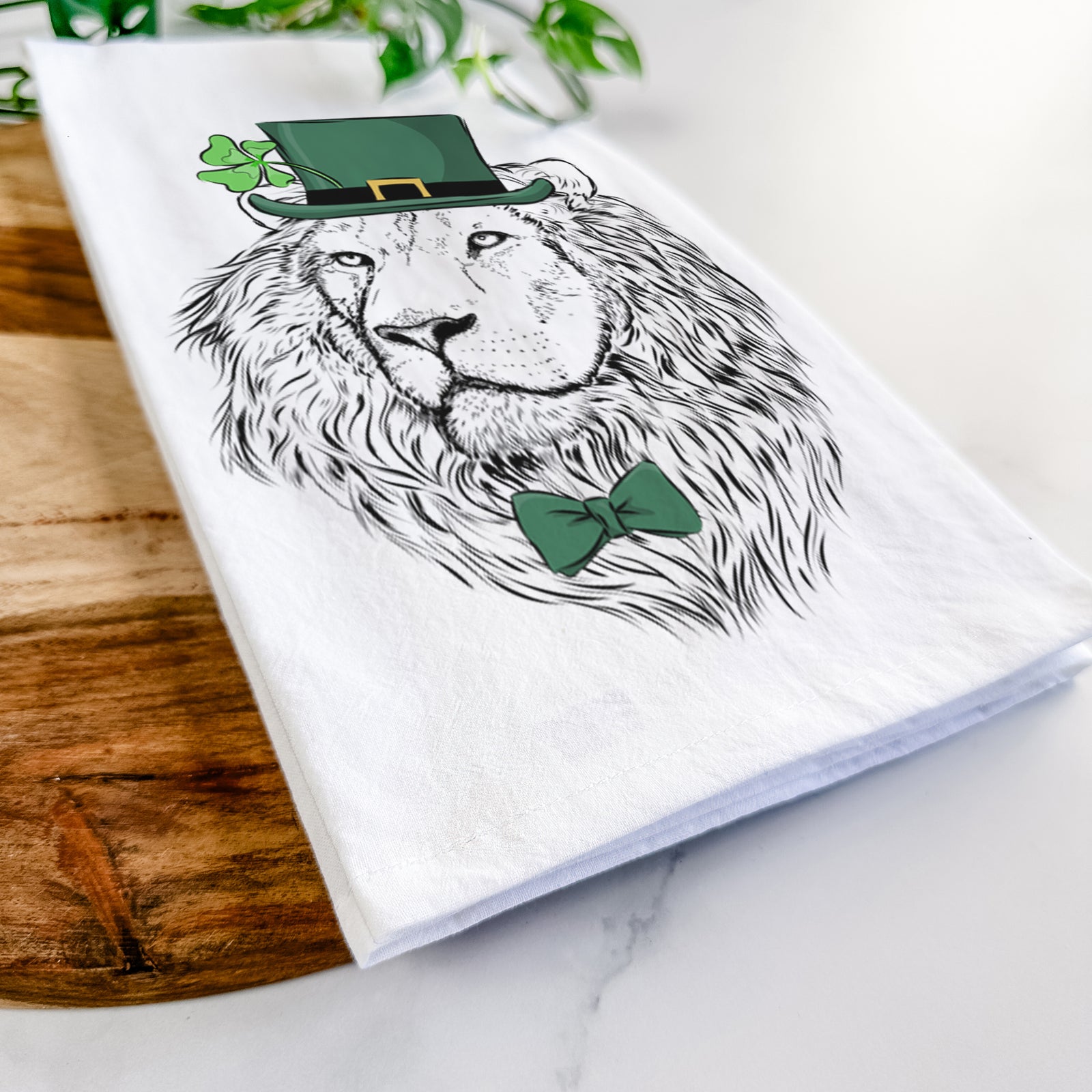 Hand-drawn sketch of Lenny the Lion wearing a St. Patrick's Day leprechaun hat and bow tie on a tea towel