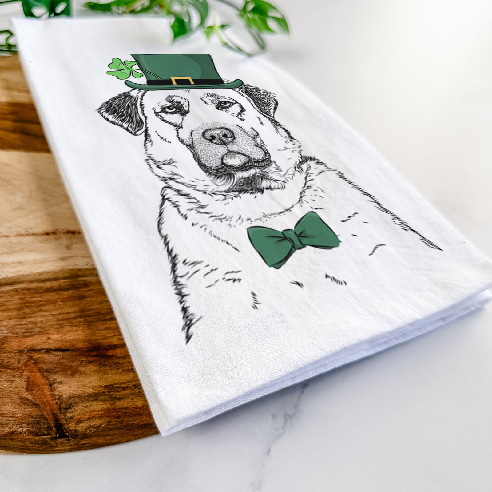 Hand-drawn sketch of Loca the Anatolian Shepherd wearing a St. Patrick's Day leprechaun hat and bow tie on a tea towel