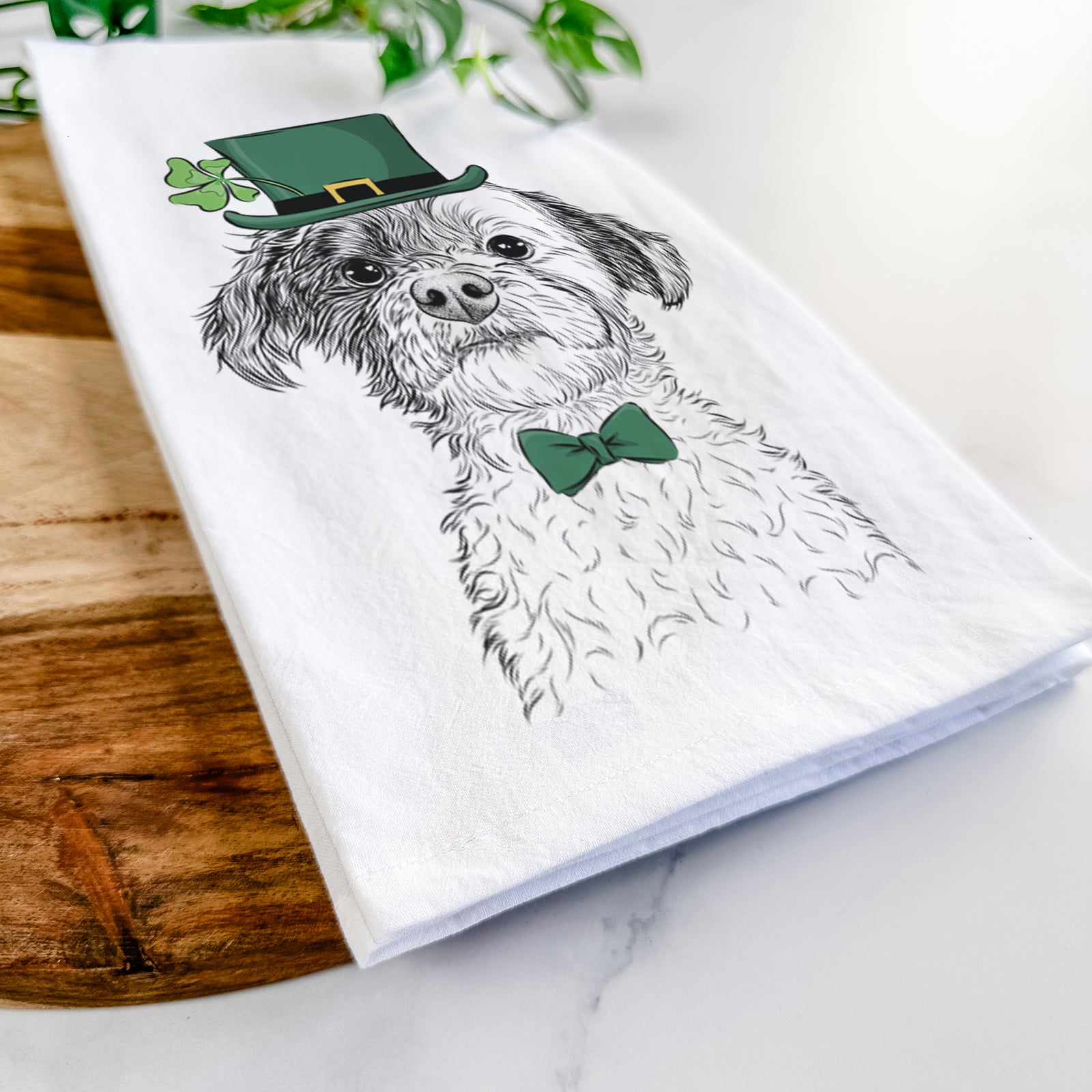 Hand-drawn sketch of Louise the Havanese wearing a St. Patrick's Day leprechaun hat and bow tie on a tea towel