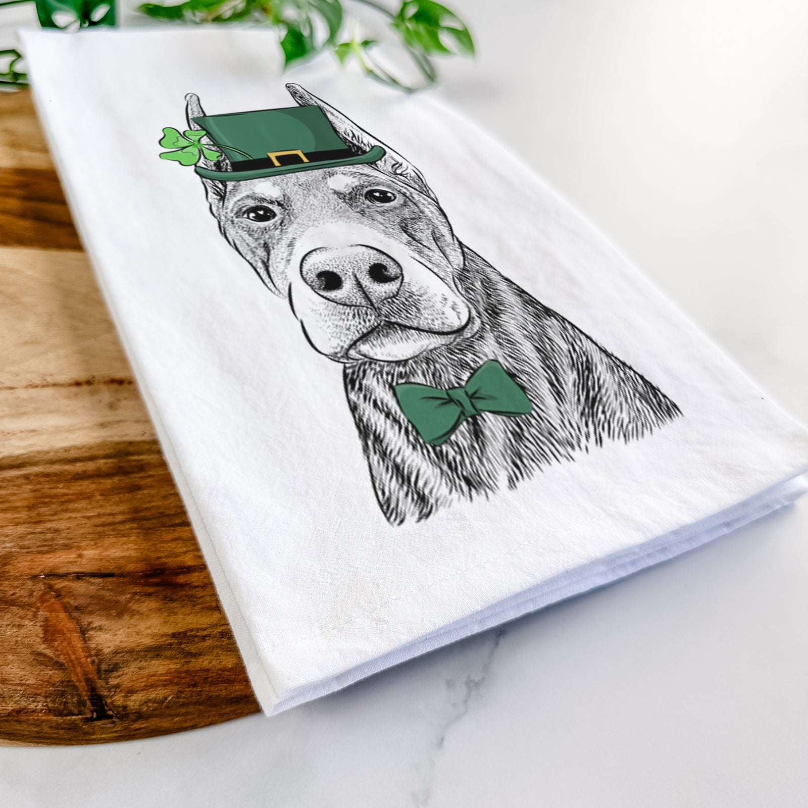 Hand-drawn sketch of Luna the Doberman Pinscher wearing a St. Patrick's Day leprechaun hat and bow tie on a tea towel