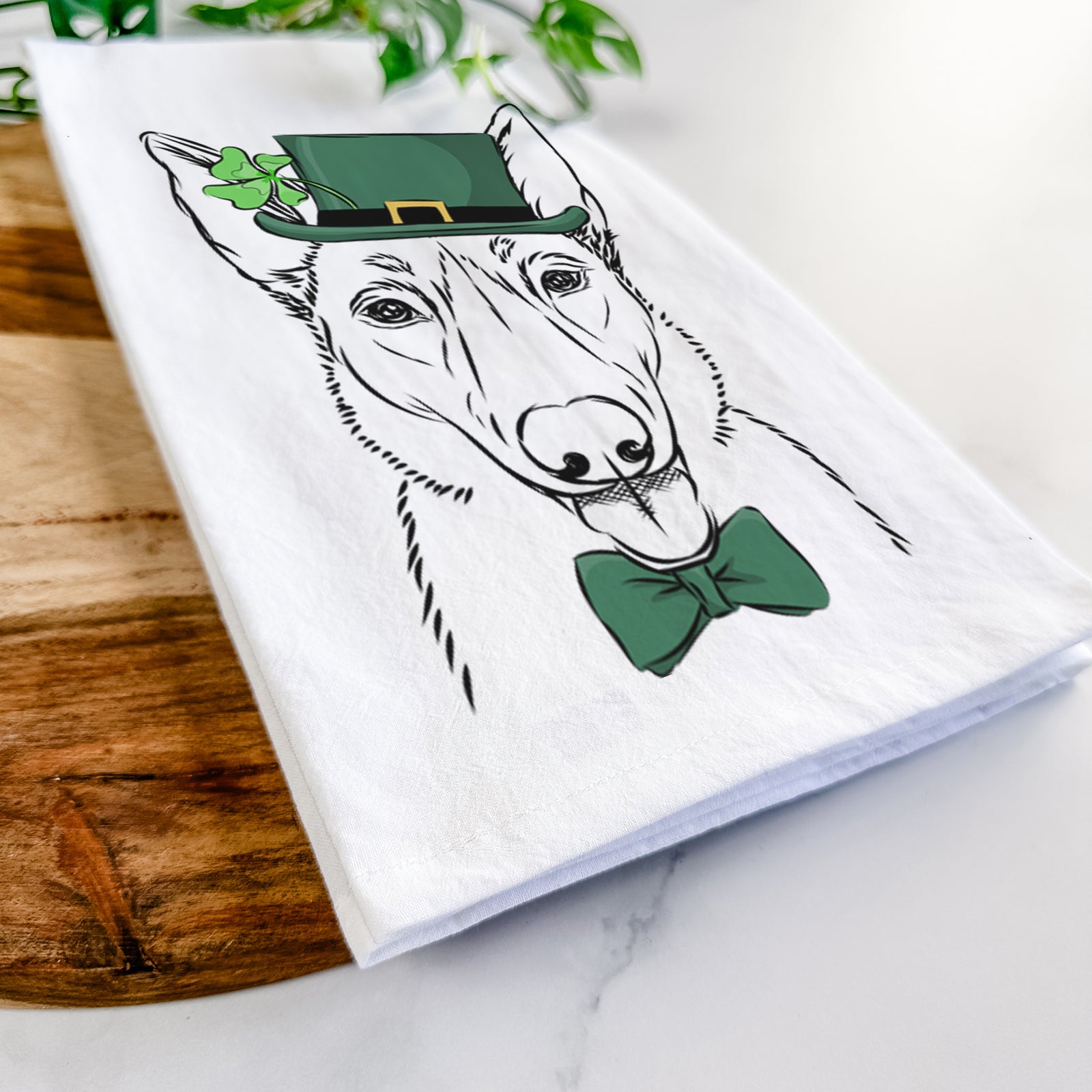 Hand-drawn sketch of Lyric the Belgian Malinois wearing a St. Patrick's Day leprechaun hat and bow tie on a tea towel
