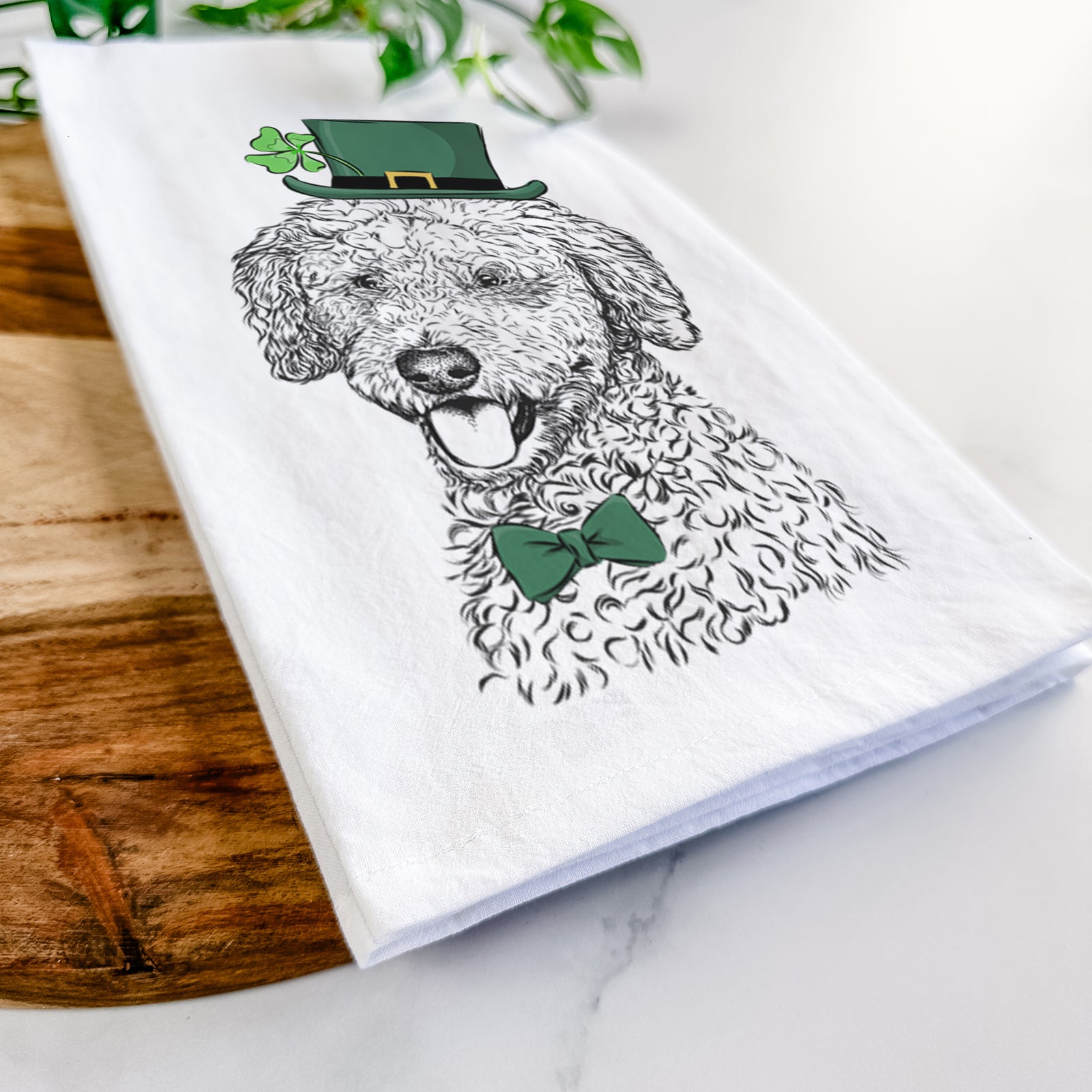 Hand-drawn sketch of Marlow the Goldendoodle wearing a St. Patrick's Day leprechaun hat and bow tie on a tea towel