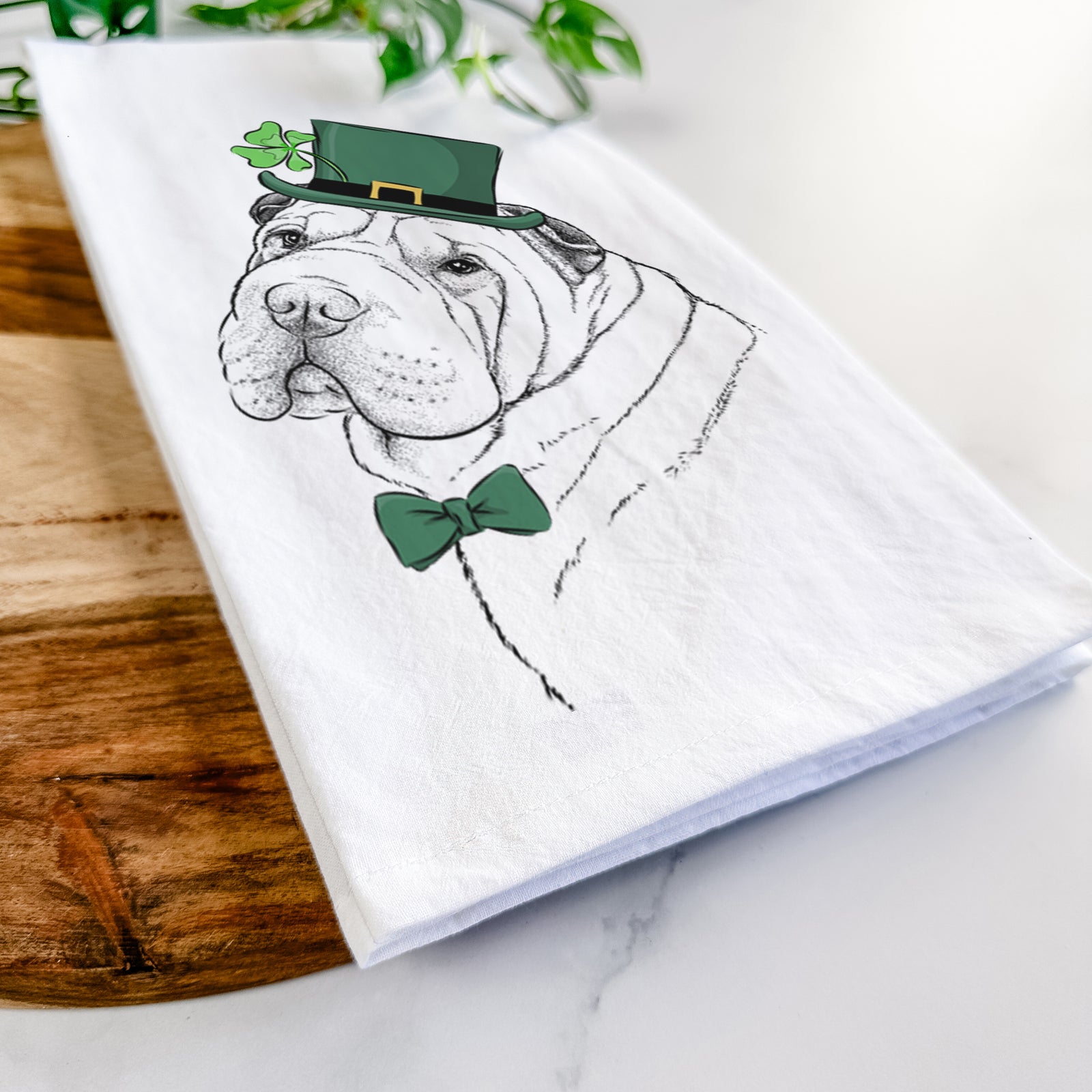 Hand-drawn sketch of Maximus the Shar Pei wearing a St. Patrick's Day leprechaun hat and bow tie on a tea towel
