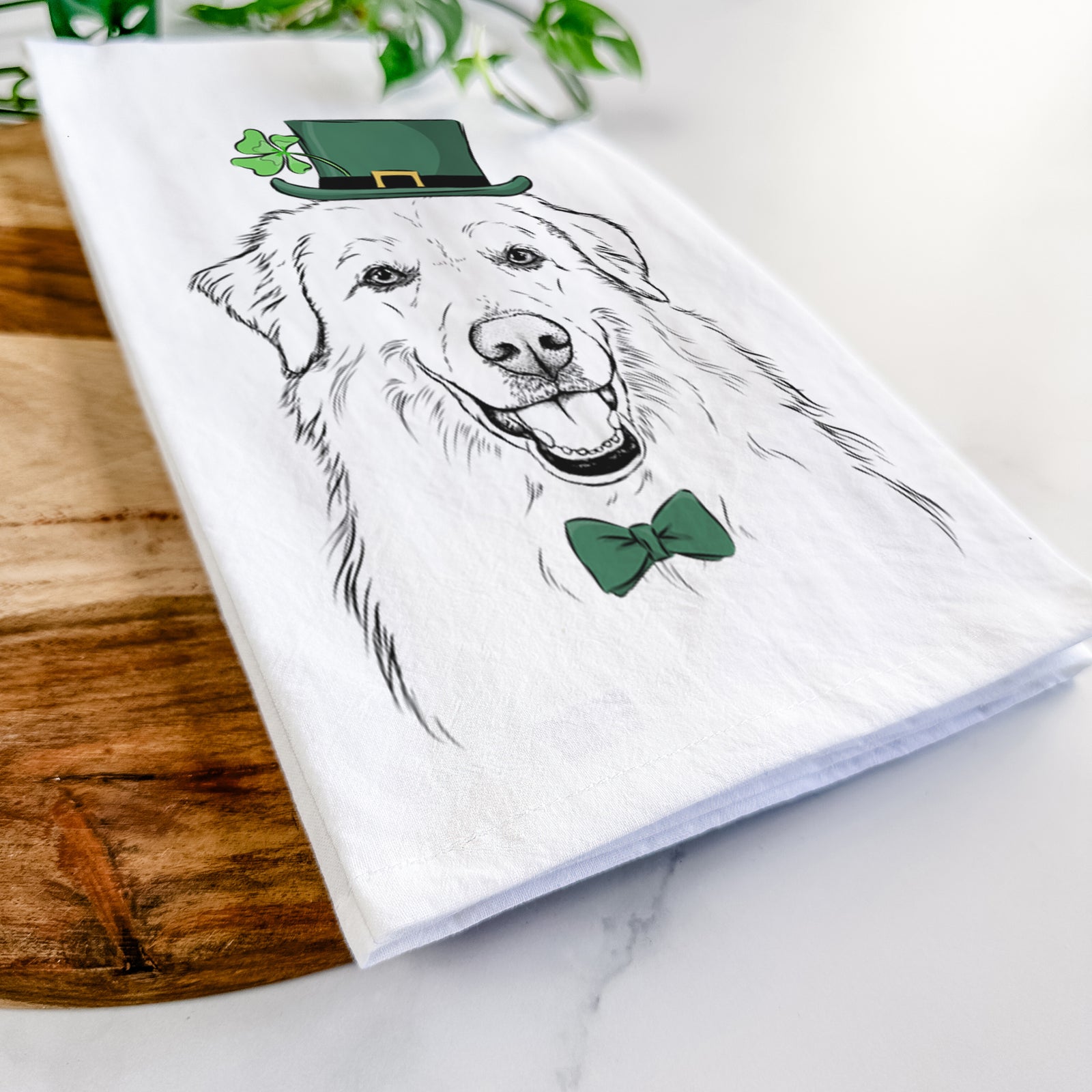 Hand-drawn sketch of Meg the Great Pyrenees wearing a St. Patrick's Day leprechaun hat and bow tie on a tea towel