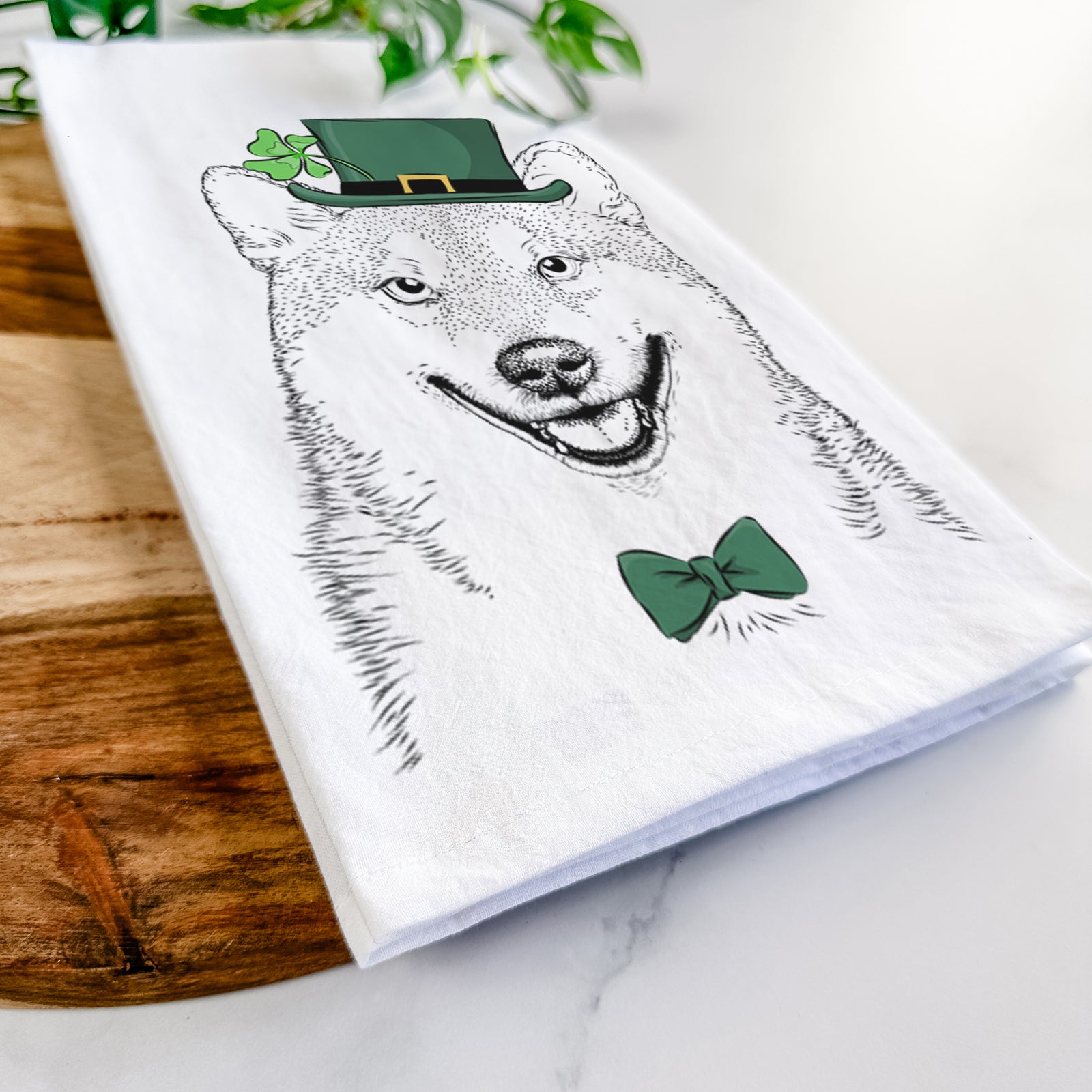 Hand-drawn sketch of Mitsu the Shiba Inu wearing a St. Patrick's Day leprechaun hat and bow tie on a tea towel