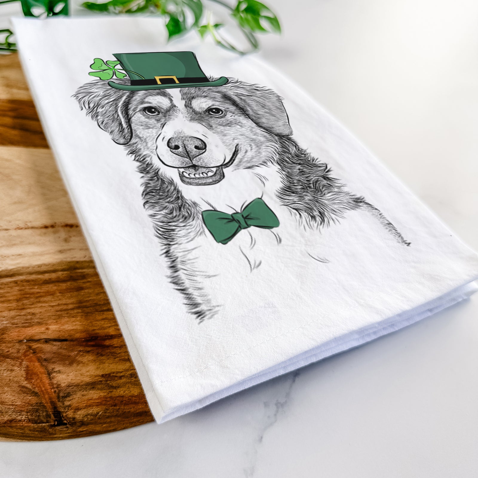 Hand-drawn sketch of Molly the Miniature Bernedoodle wearing a St. Patrick's Day leprechaun hat and bow tie on a tea towel