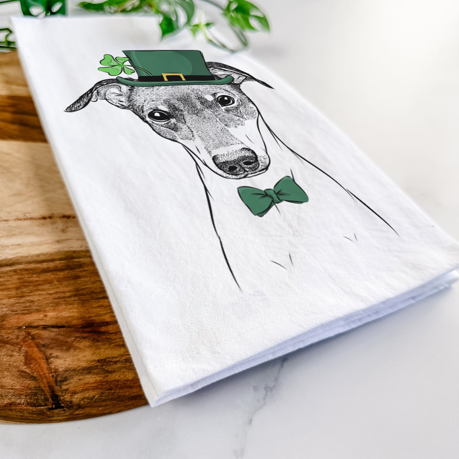 Hand-drawn sketch of Momo the Japanese Terrier wearing a St. Patrick's Day leprechaun hat and bow tie on a tea towel