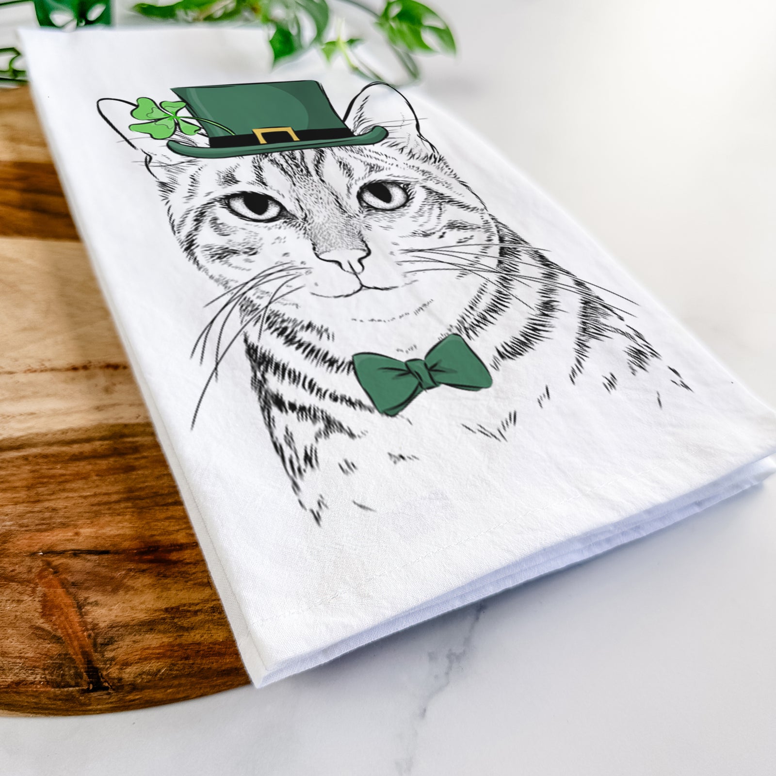 Hand-drawn sketch of Nell the Tabby Cat wearing a St. Patrick's Day leprechaun hat and bow tie on a tea towel