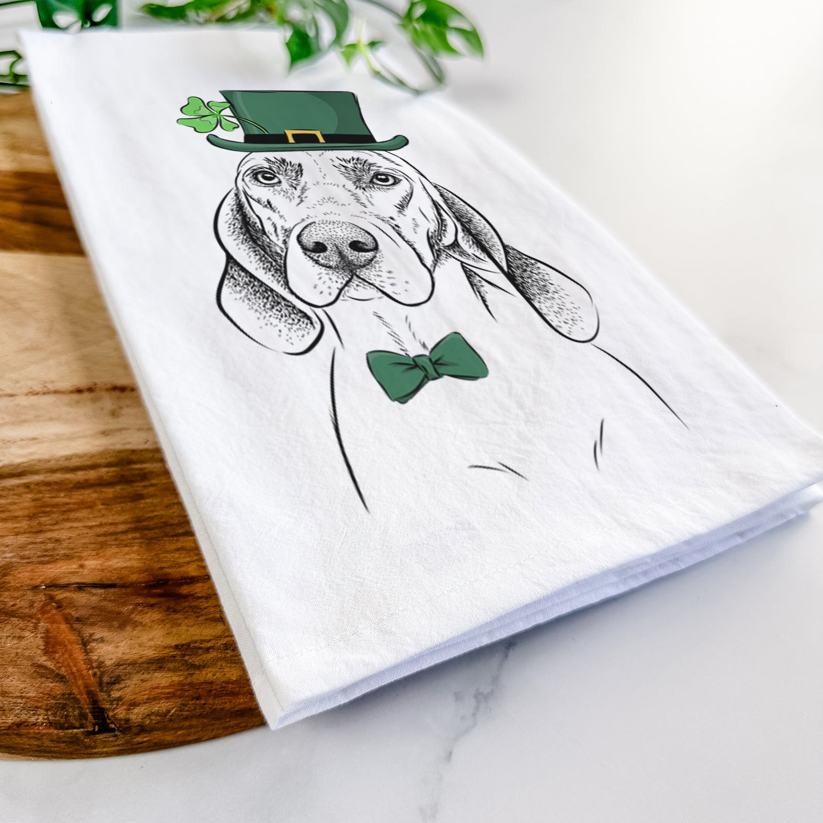 Hand-drawn sketch of Norman the Plott Hound wearing a St. Patrick's Day leprechaun hat and bow tie on a tea towel