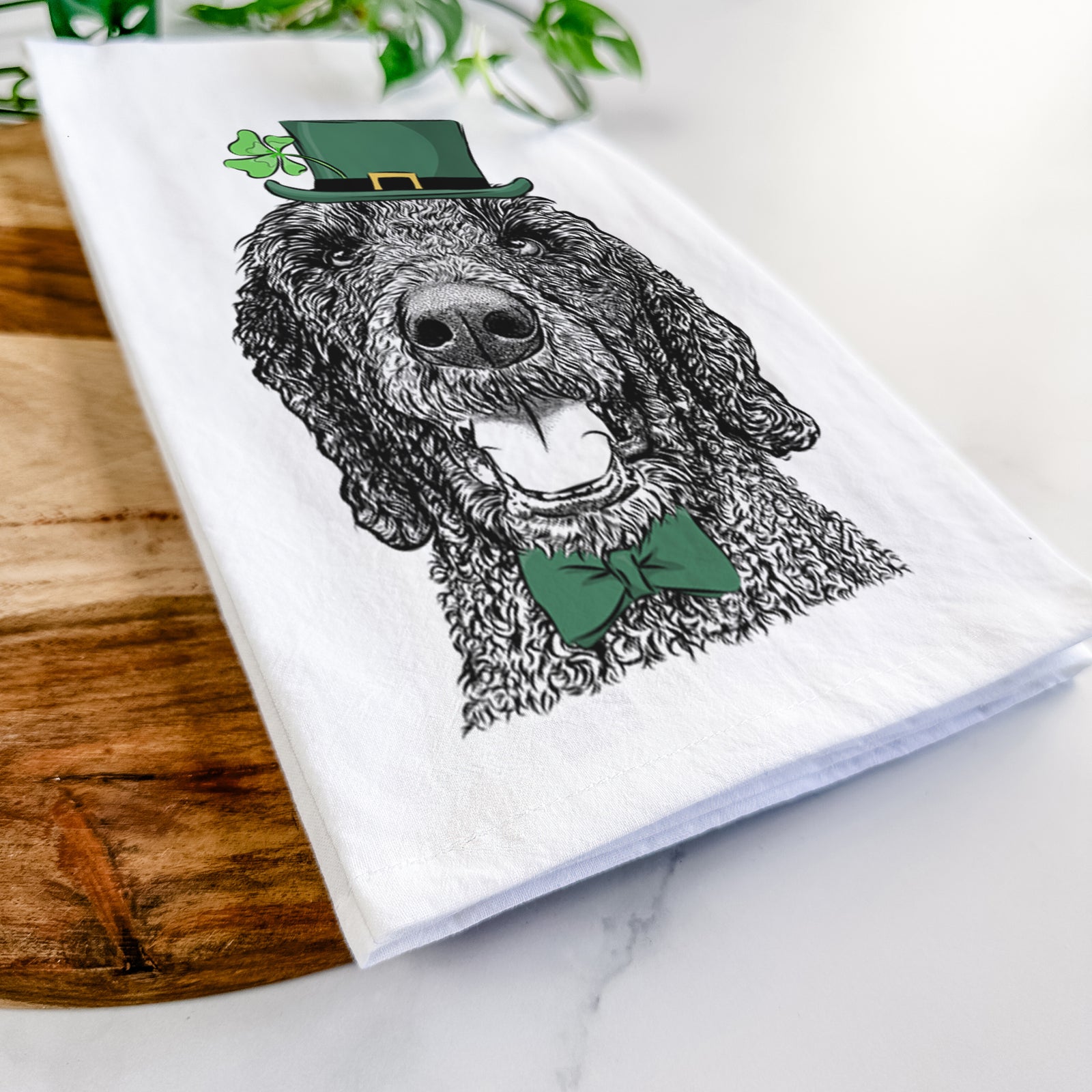 Hand-drawn sketch of Obi James the Goldendoodle wearing a St. Patrick's Day leprechaun hat and bow tie on a tea towel