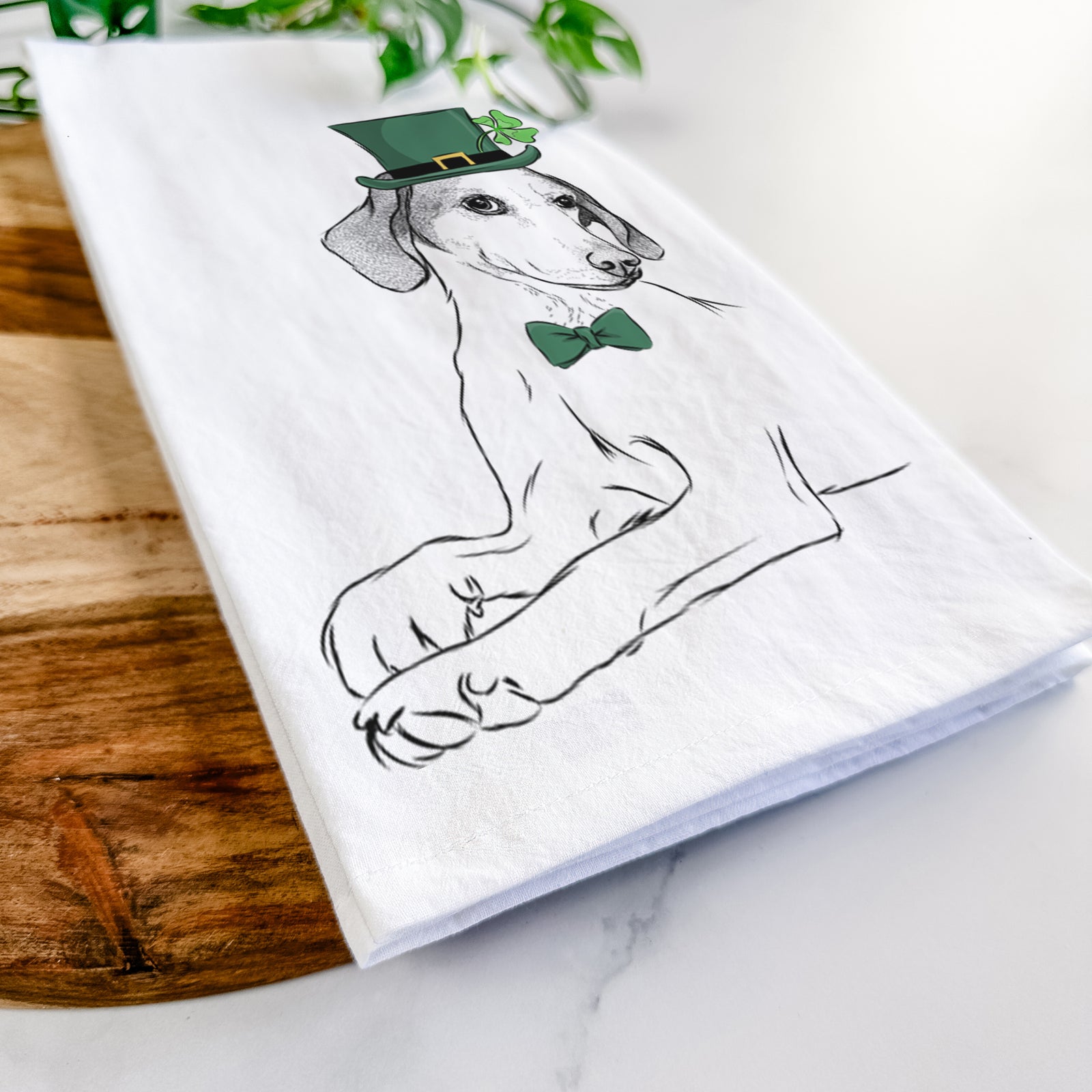 Hand-drawn sketch of Opie the Foxhound wearing a St. Patrick's Day leprechaun hat and bow tie on a tea towel