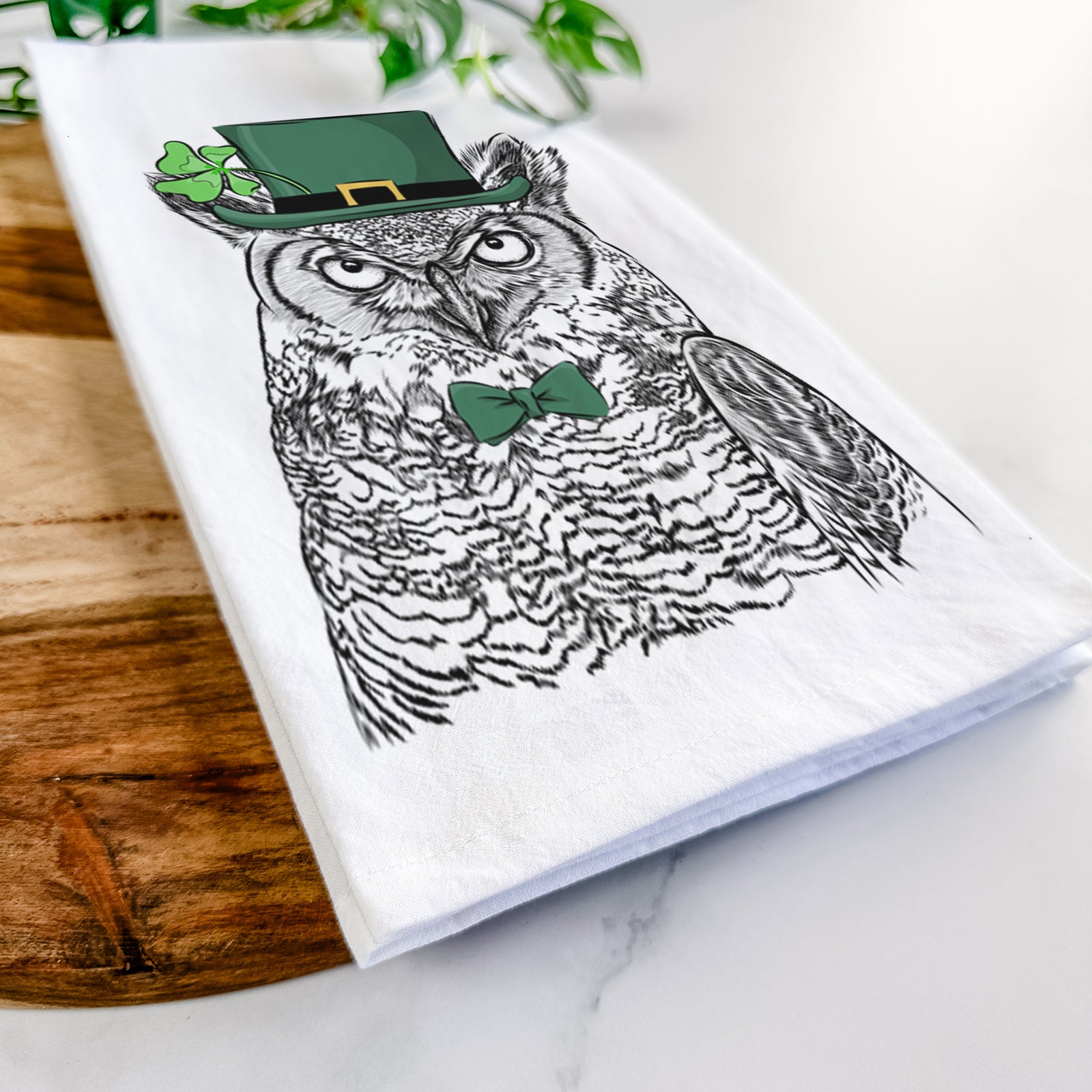 Hand-drawn sketch of Ozwald the Grey Horned Owl wearing a St. Patrick's Day leprechaun hat and bow tie on a tea towel