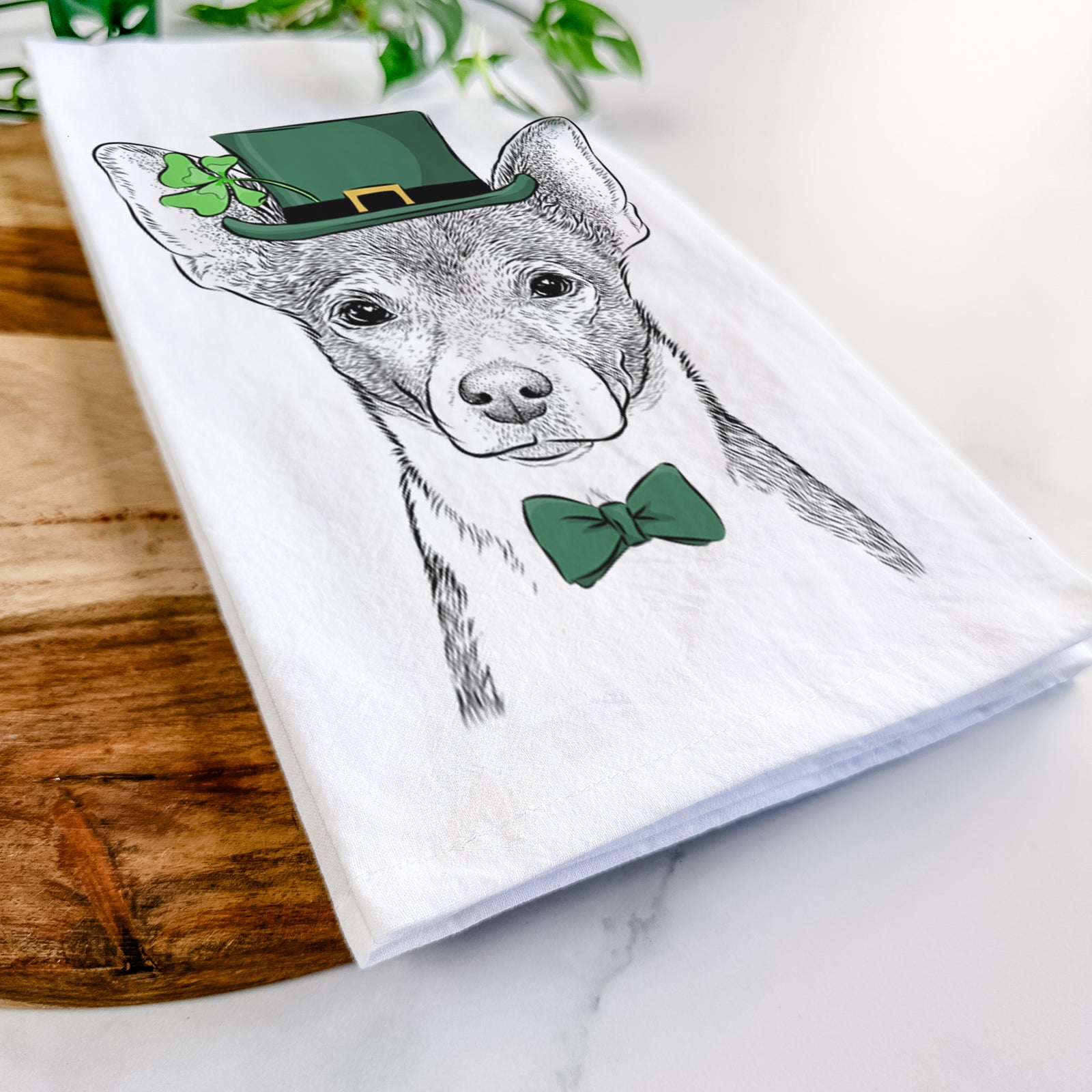 Hand-drawn sketch of Peanut the Chihuahua wearing a St. Patrick's Day leprechaun hat and bow tie on a tea towel