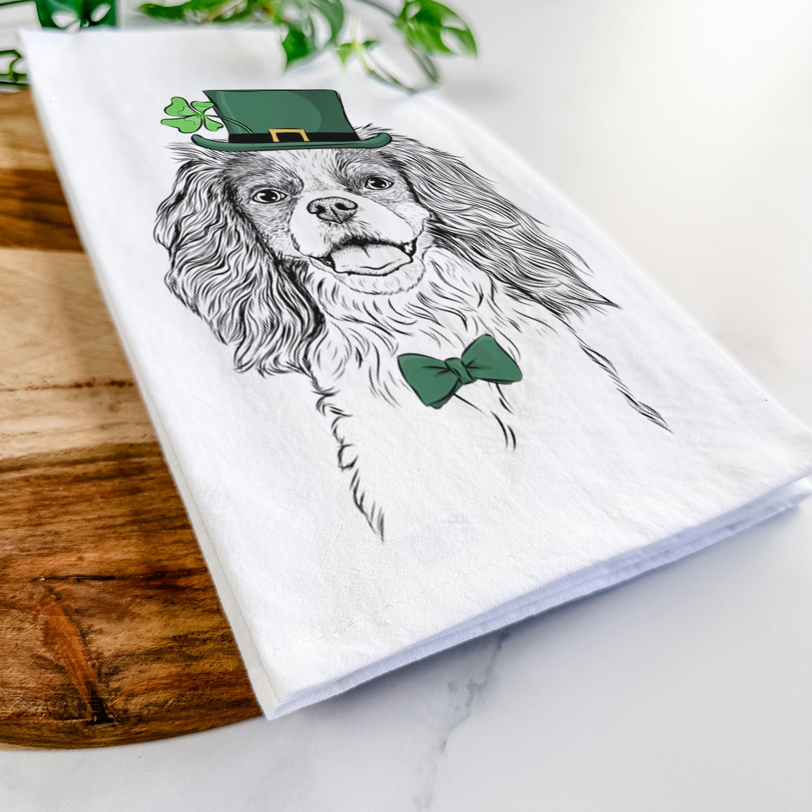 Hand-drawn sketch of Poppy the Cavalier King Charles Spaniel wearing a St. Patrick's Day leprechaun hat and bow tie on a tea towel
