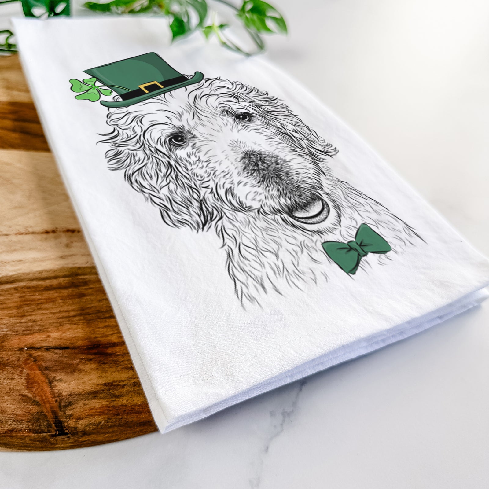 Hand-drawn sketch of Preston the Labradoodle wearing a St. Patrick's Day leprechaun hat and bow tie on a tea towel