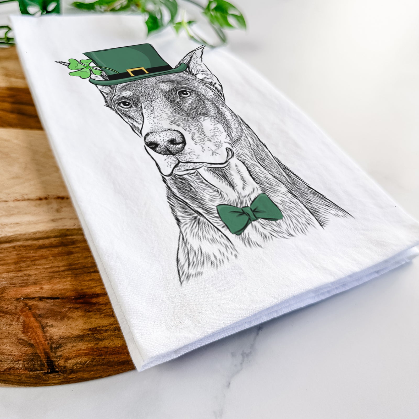 Hand-drawn sketch of RJ the Doberman Pinscher wearing a St. Patrick's Day leprechaun hat and bow tie on a tea towel
