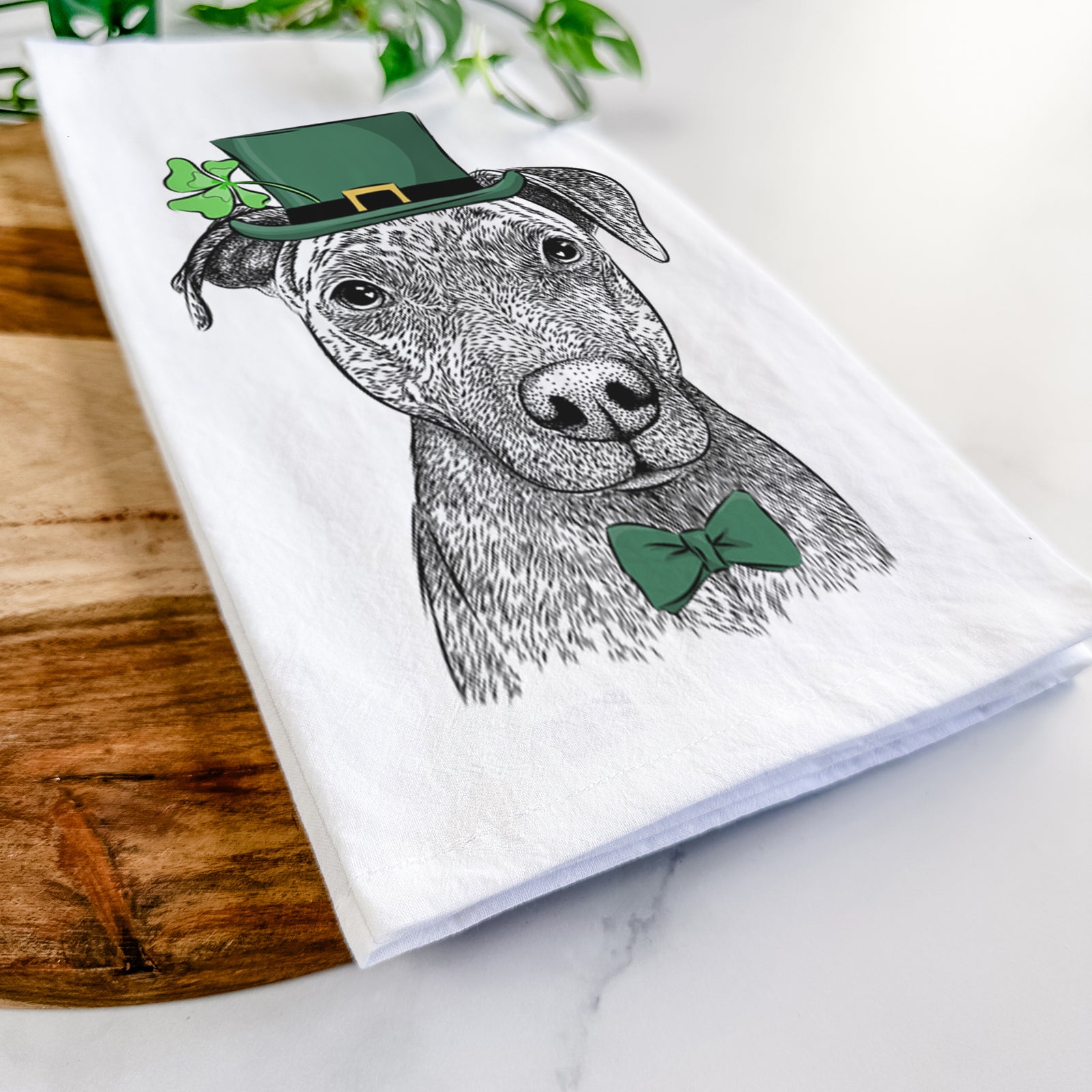 Hand-drawn sketch of Reeses the Pitbull wearing a St. Patrick's Day leprechaun hat and bow tie on a tea towel