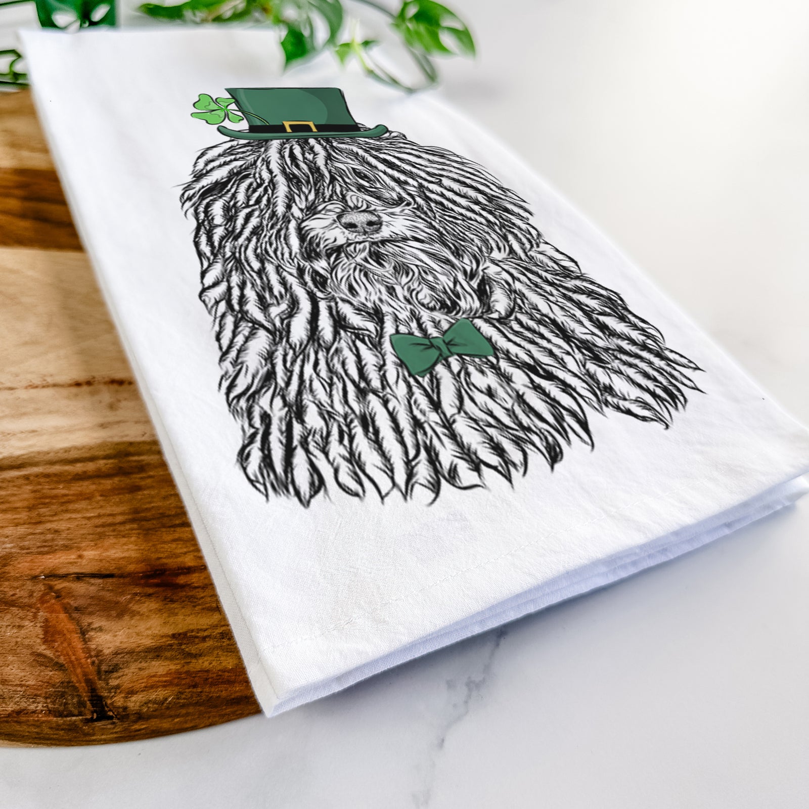 Hand-drawn sketch of Rezi the Puli wearing a St. Patrick's Day leprechaun hat and bow tie on a tea towel