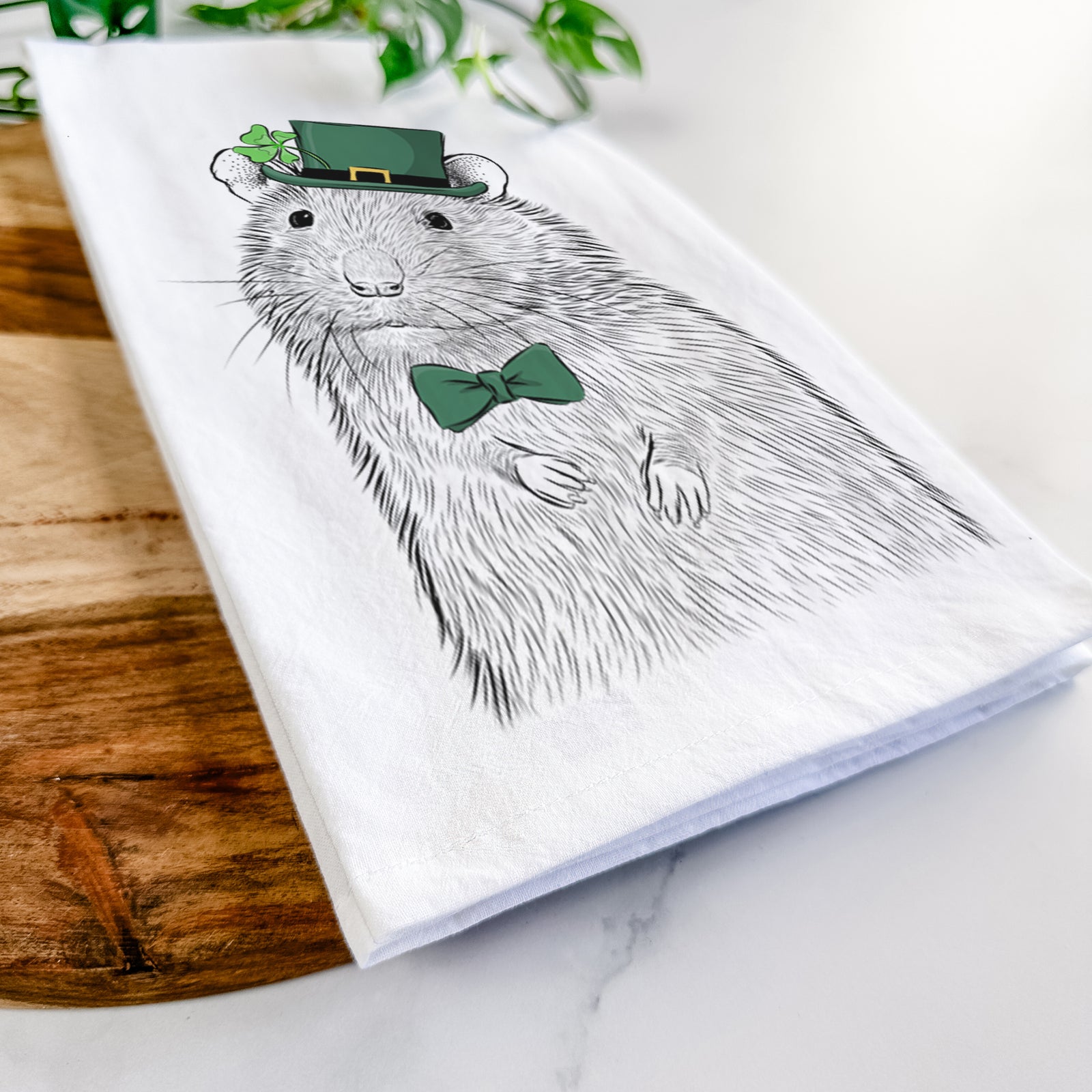 Hand-drawn sketch of Rizzo the Rat wearing a St. Patrick's Day leprechaun hat and bow tie on a tea towel